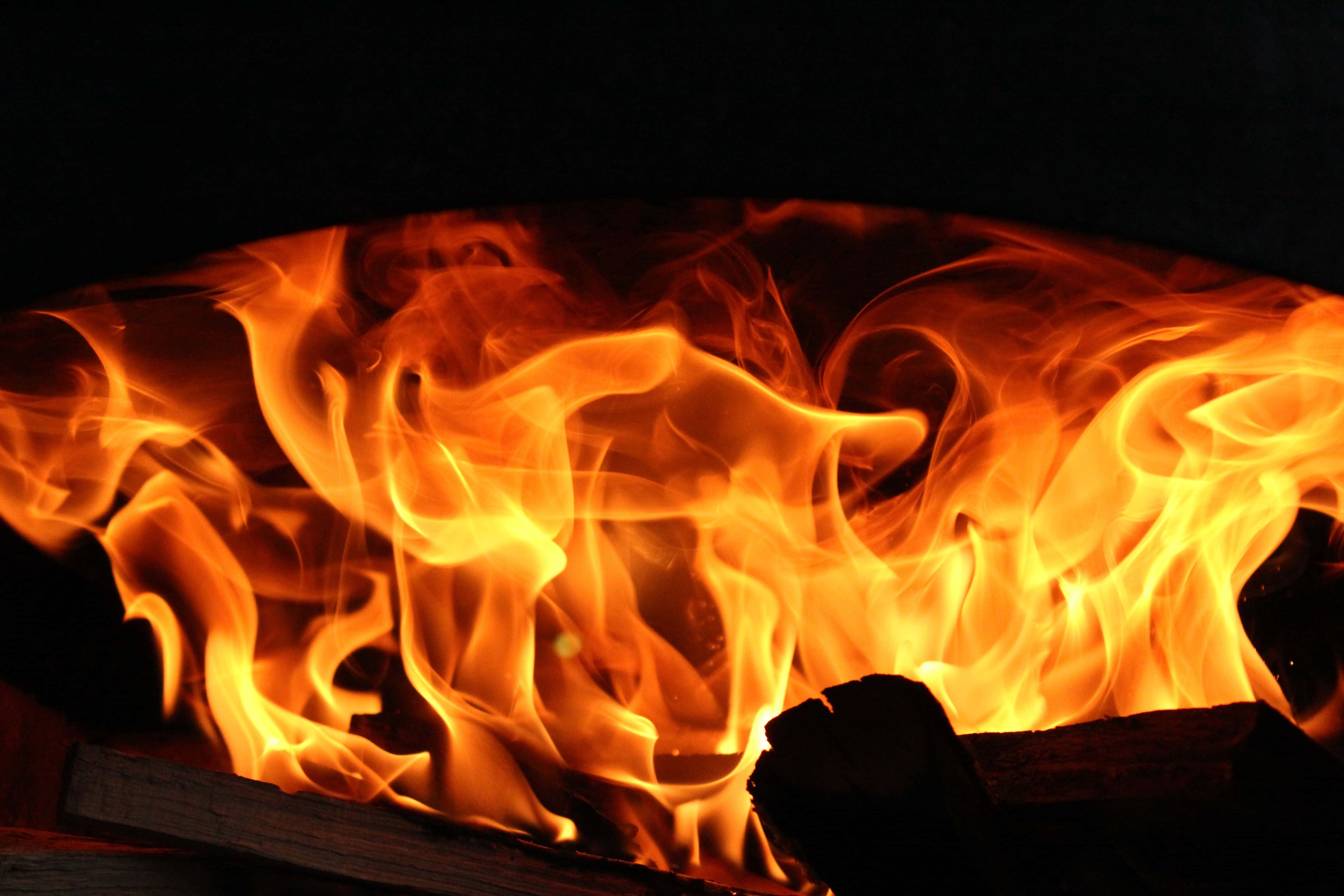 Cozy Fire 桌布 壁紙 — 鮮豔的橙色和黃色火焰在漆黑的背景上動態舞動，伴隨著發光的餘燼和燒焦的木頭。