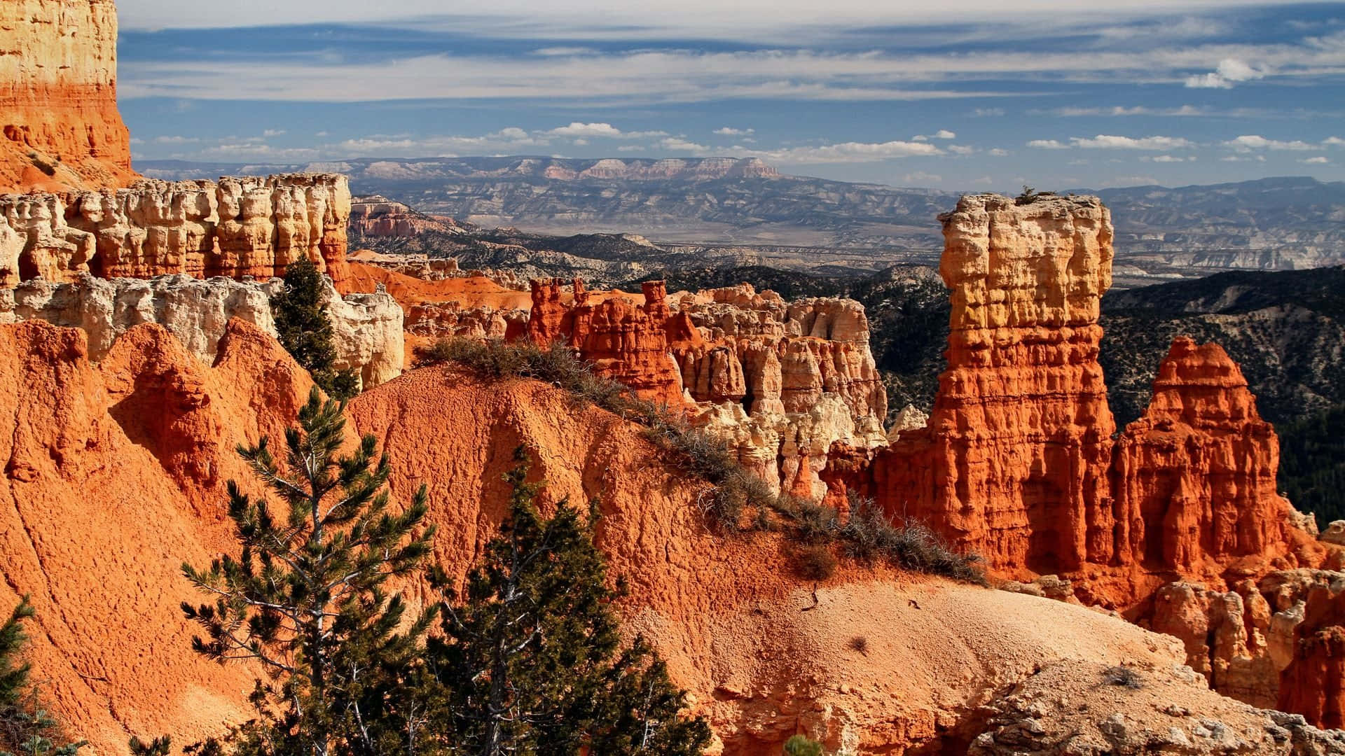 Utah 桌布 壁紙 — 鮮豔的橙色岩柱在廣闊的沙漠峽谷中，在藍天白雲的映襯下戲劇性地聳立。