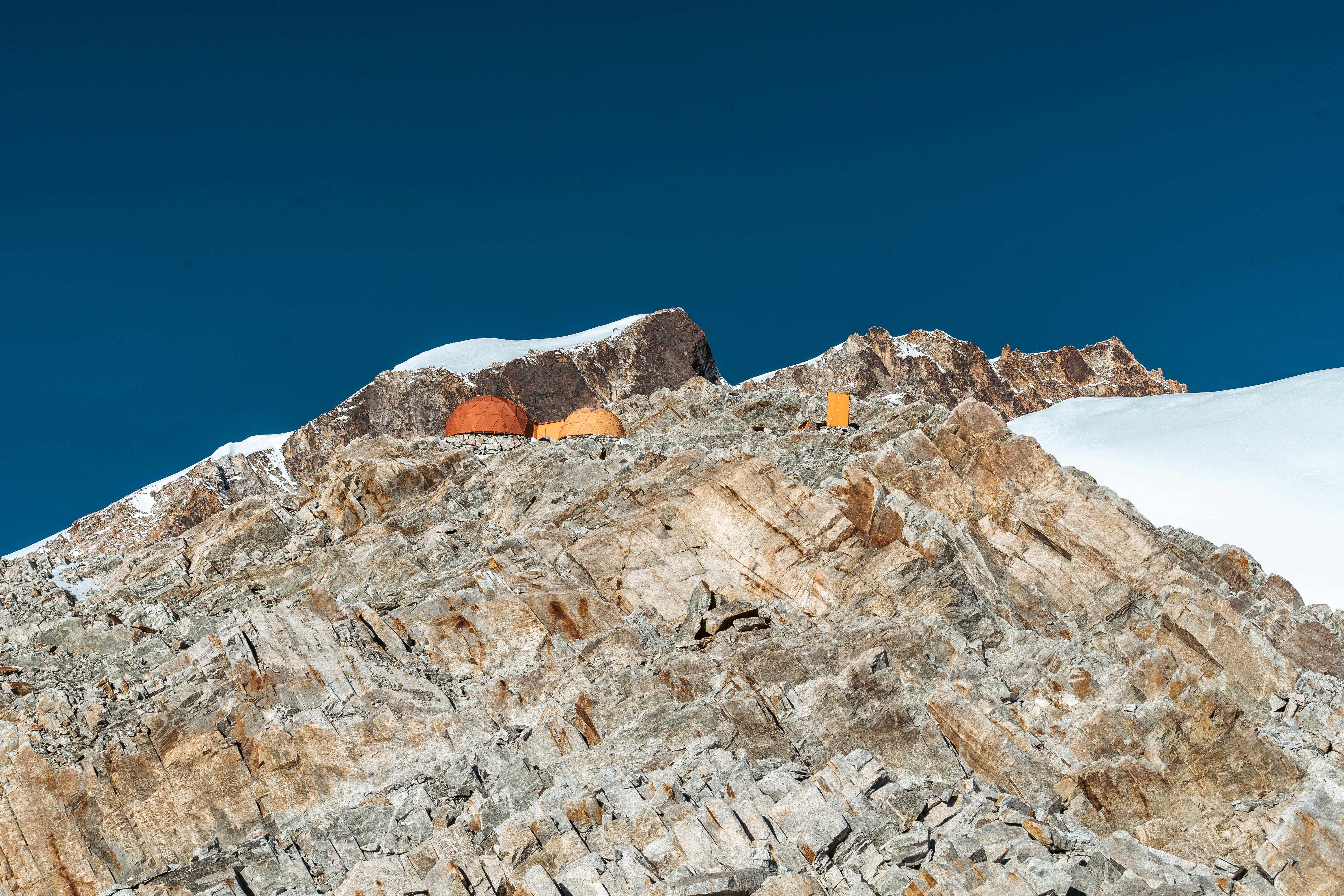 Bolivia 桌布 壁紙 — 鮮豔的橙色帳篷坐落在崎嶇積雪的山脊上，背景是深藍色的天空。