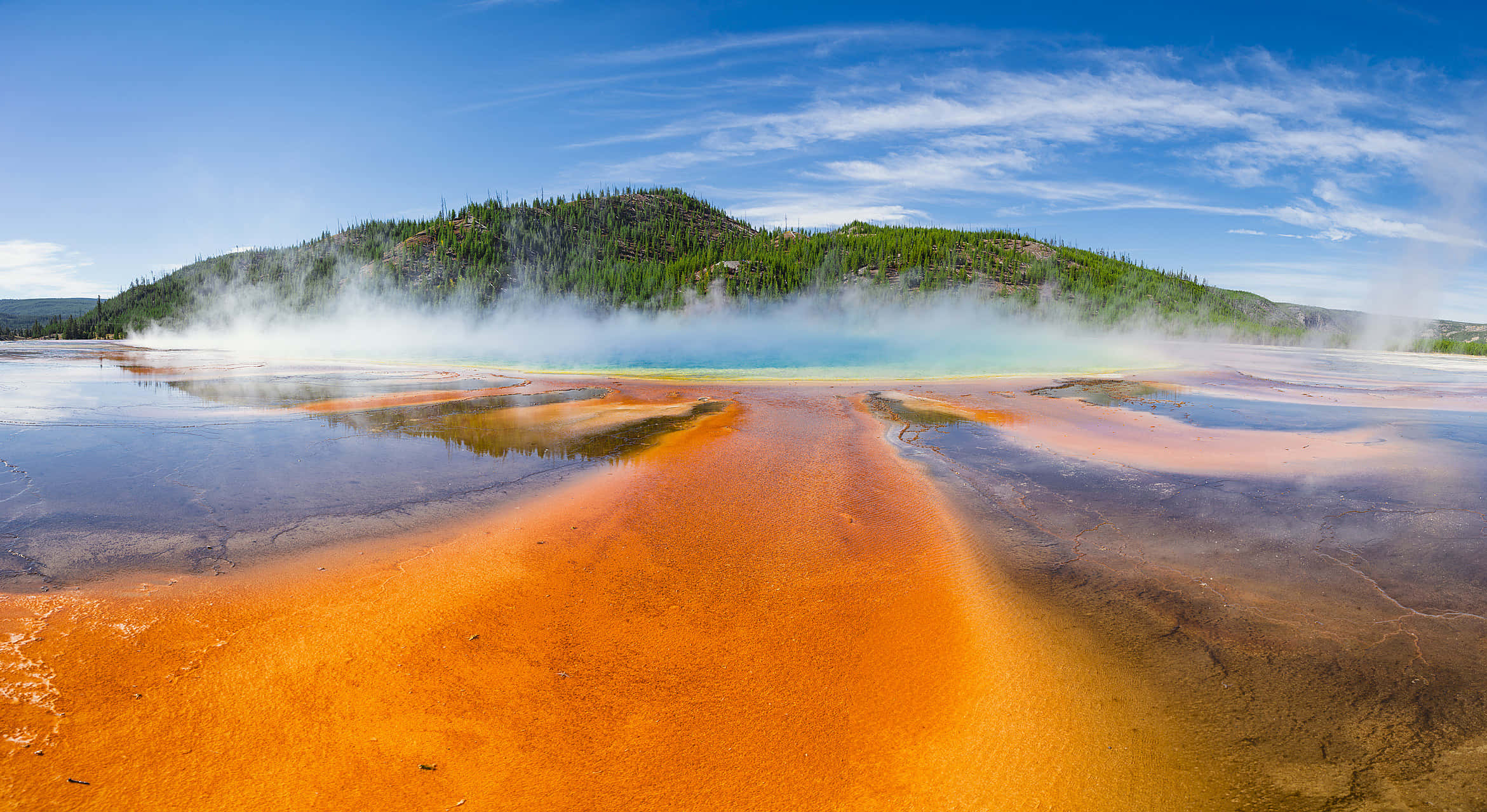 Yellowstone 桌布 壁紙 — 鮮豔的橙色微生物墊在晴朗藍天和縷縷白雲下，於冒著蒸汽的溫泉上起伏波動。