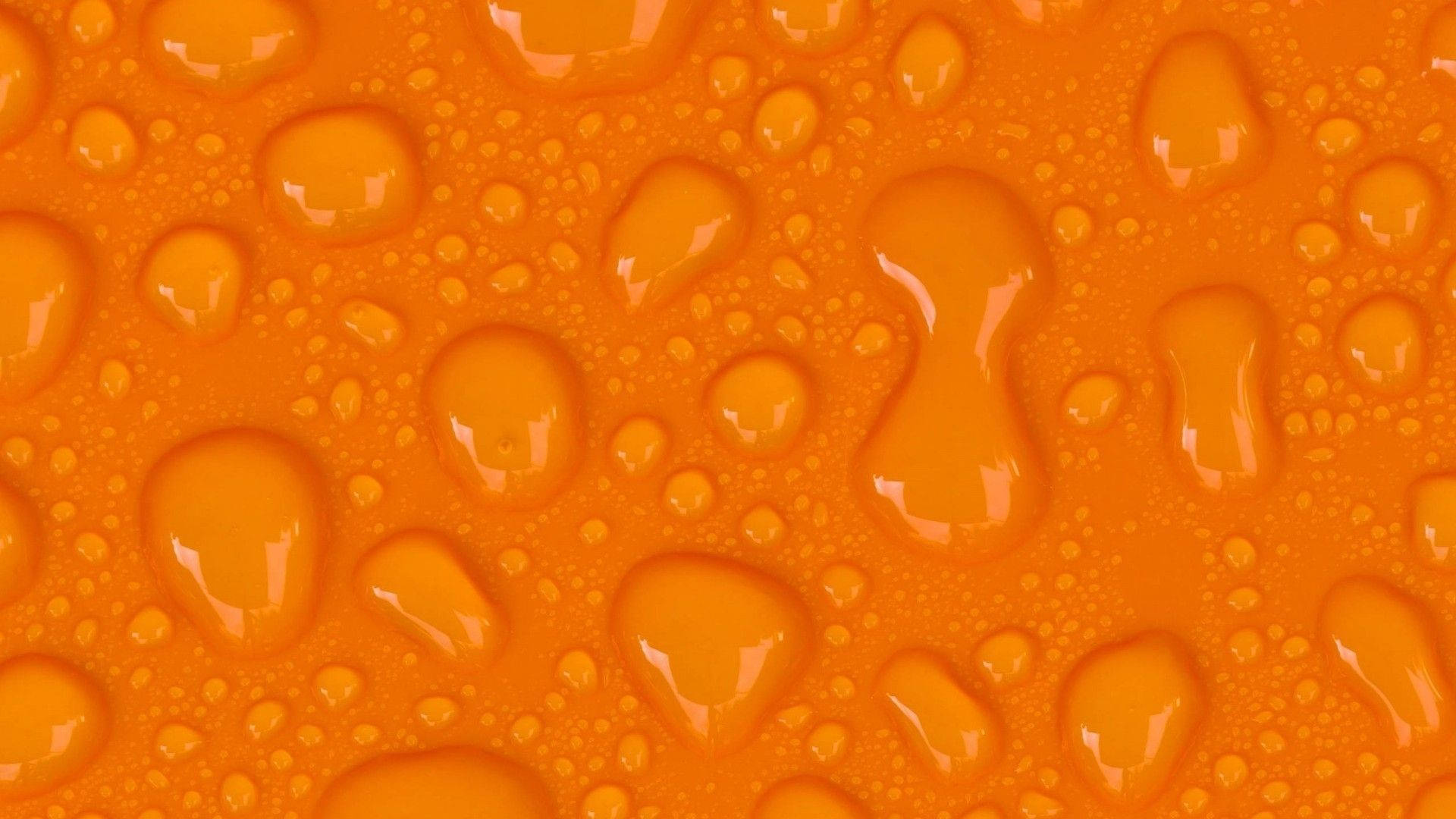 Orange 桌布 壁紙 — 鮮豔的橙色液體水滴在光滑表面上閃爍著反射，形成動態的抽象紋理。