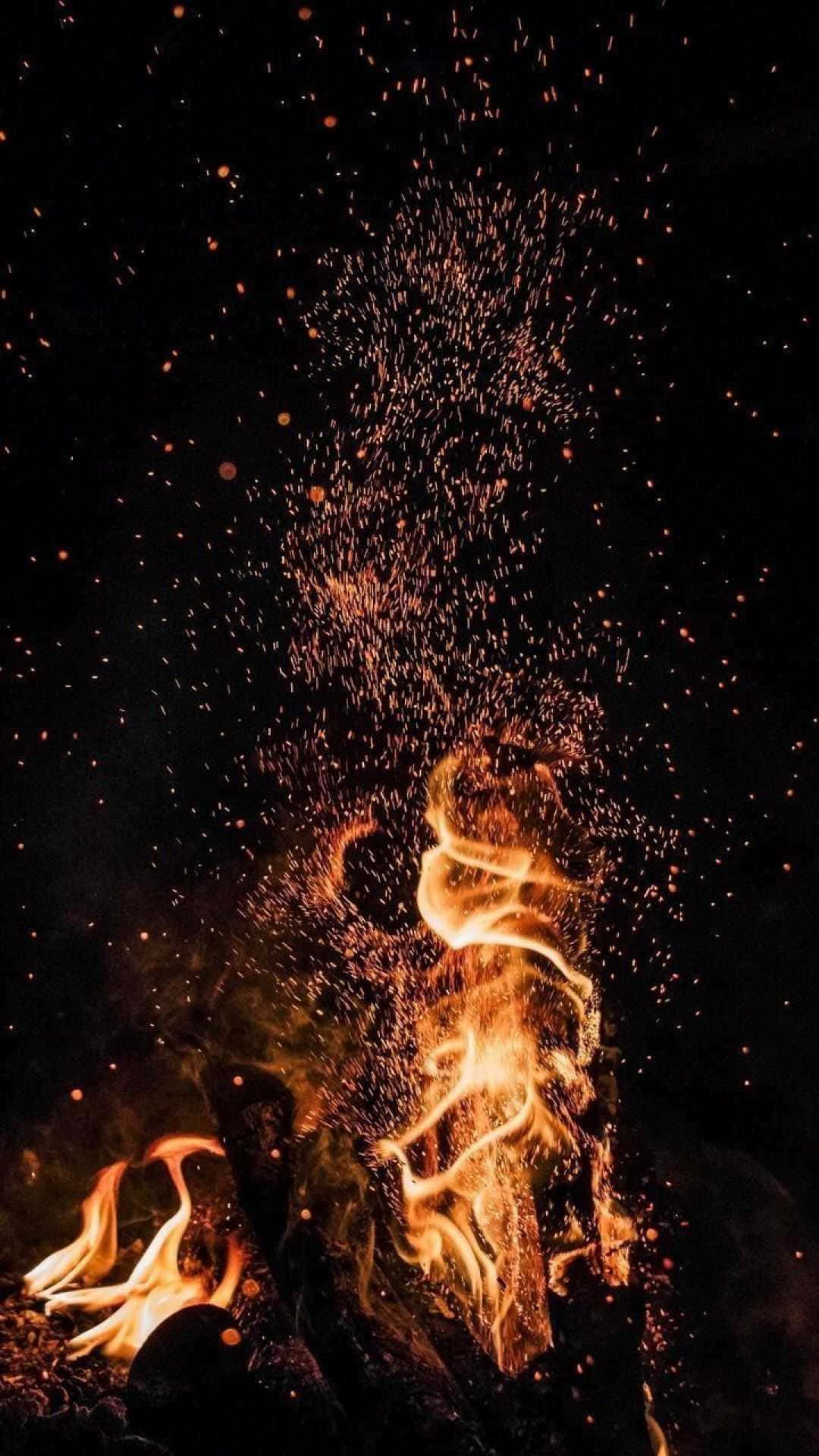 ash 桌布 壁紙 — 鮮豔的橙色火焰和發光的餘燼在漆黑的夜空中向上爆發，形成動態的火焰展示。