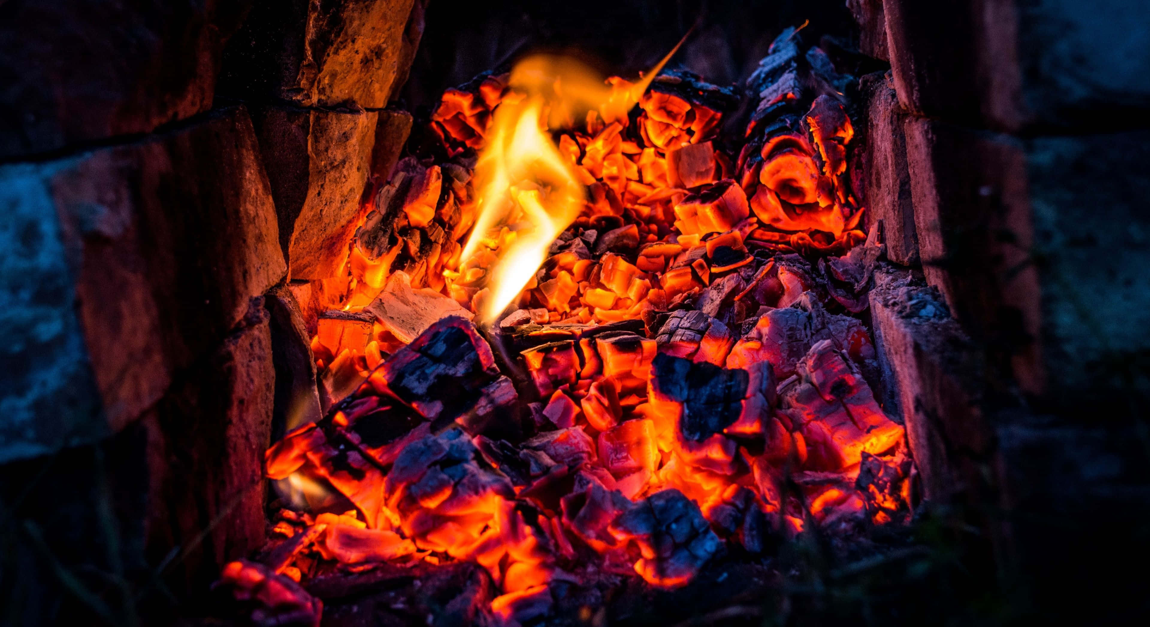 Charcoal 桌布 壁紙 — 鮮豔的橙色火焰在深色石頭中閃爍的餘燼上舞動，在舒適的夜晚環境中散發出溫暖的光芒。
