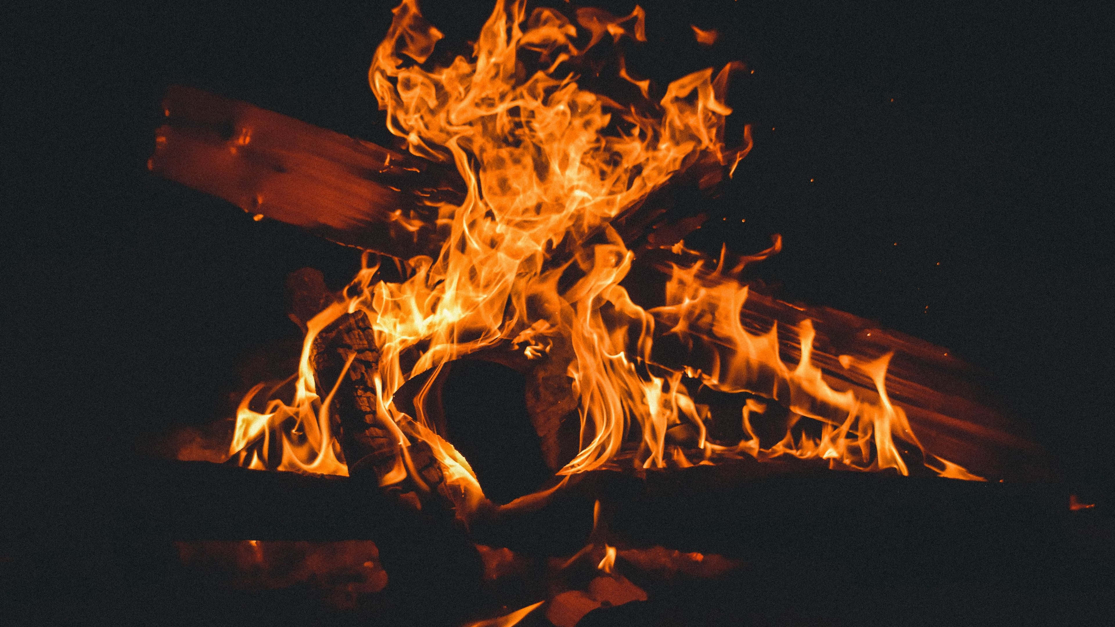 Burn 桌布 壁紙 — 鮮豔的橙色火焰在漆黑的夜空背景下，圍繞著燃燒的木柴跳躍舞動。