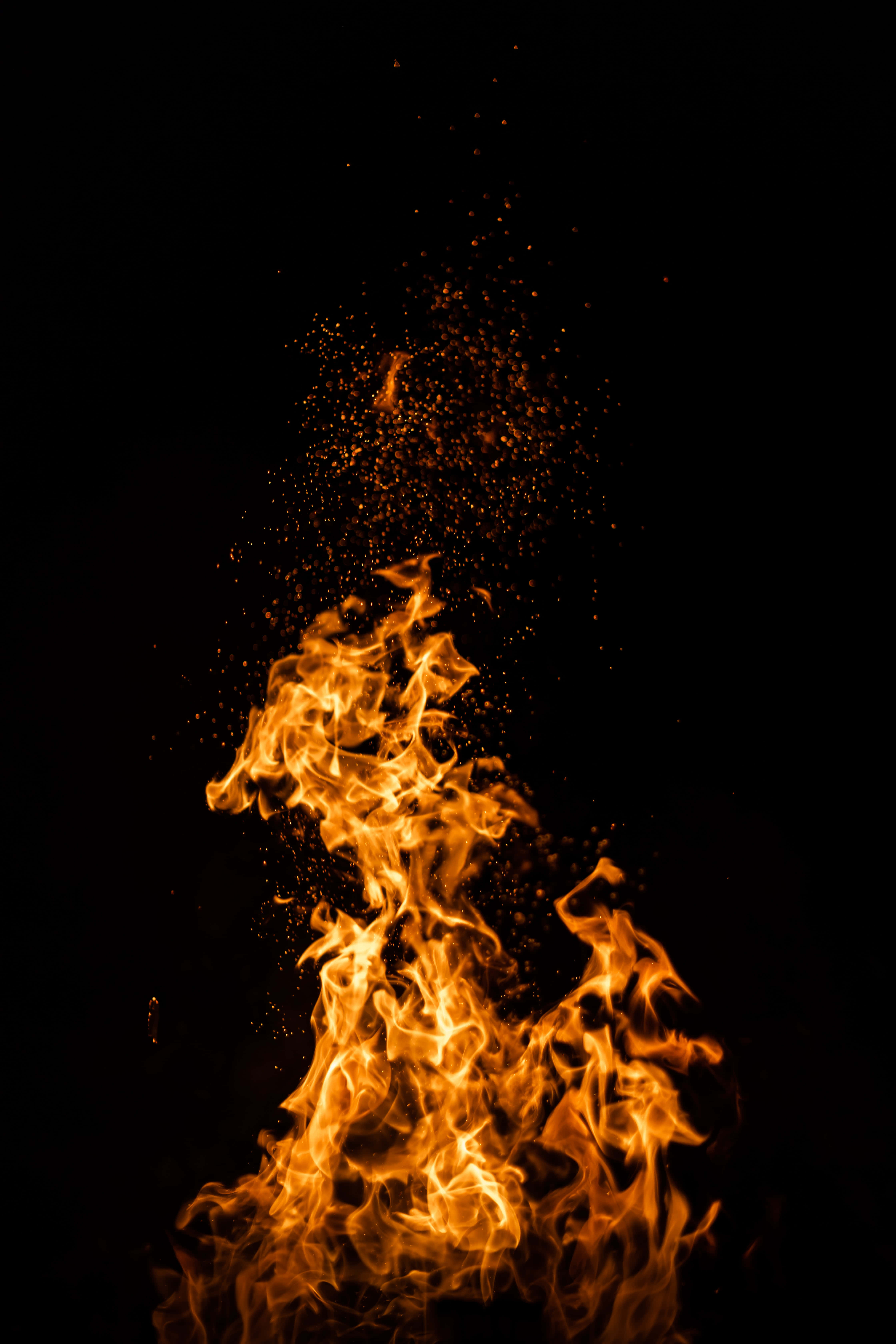 iPhone 桌布 壁紙 — 鮮豔的橙色火焰在純黑色背景上向上爆發，發光的餘燼向上飄散。