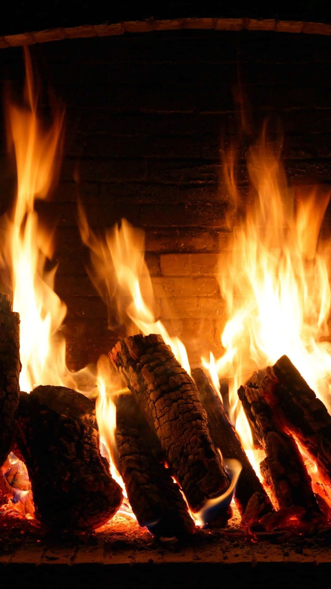 Cozy Fire 桌布 壁紙 — 鮮豔的橙色火焰從黑暗磚砌壁爐內劈啪作響的木柴中躍起，散發出溫暖的光芒。