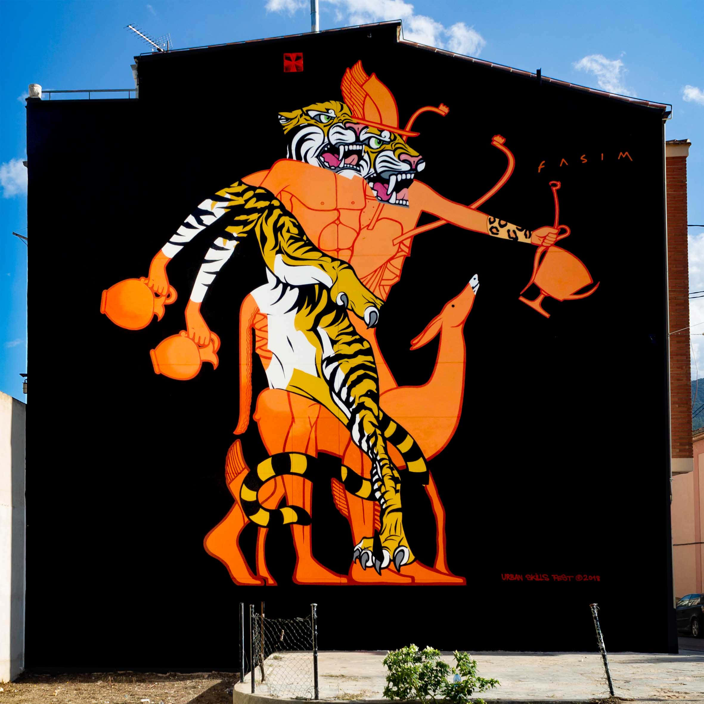 Graffiti Art 桌布 壁紙 — 鮮豔的橙色老虎壁畫，帶有火焰頭飾和水壺道具，在晴朗的藍天下佔據了黑色的城市牆壁。