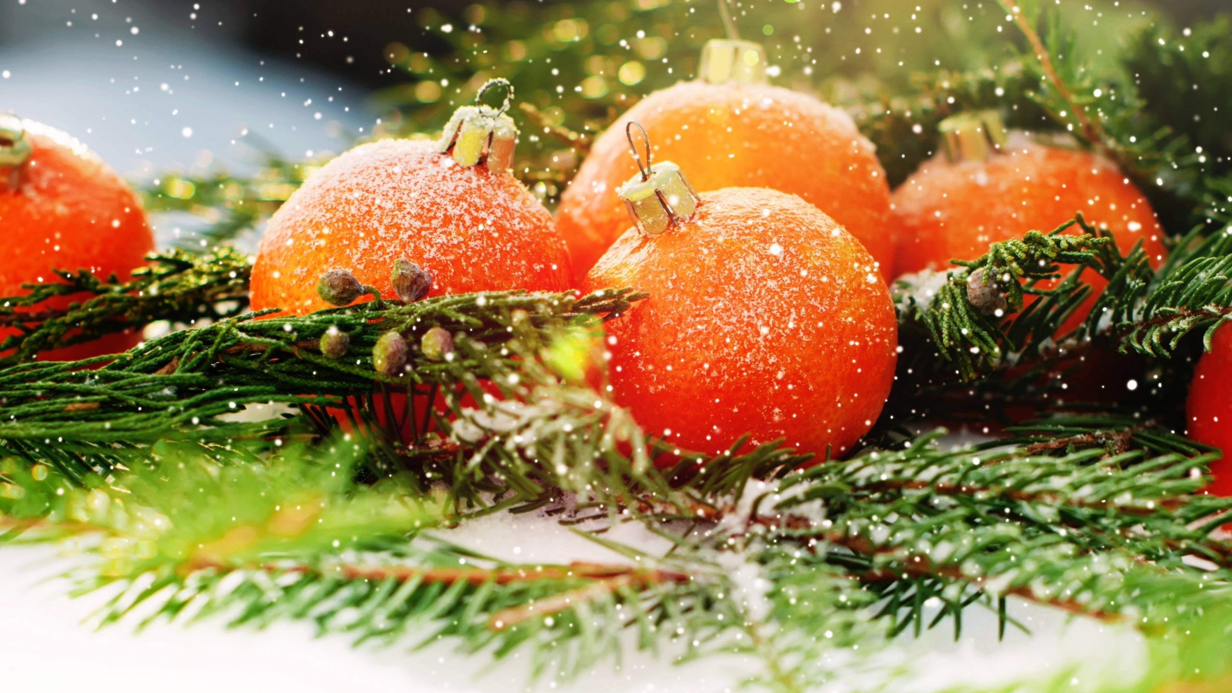 balls 桌布 壁紙 — 鮮豔的橙色聖誕裝飾品上灑滿雪花，在飄落的雪花下靜置於綠色松枝之間。