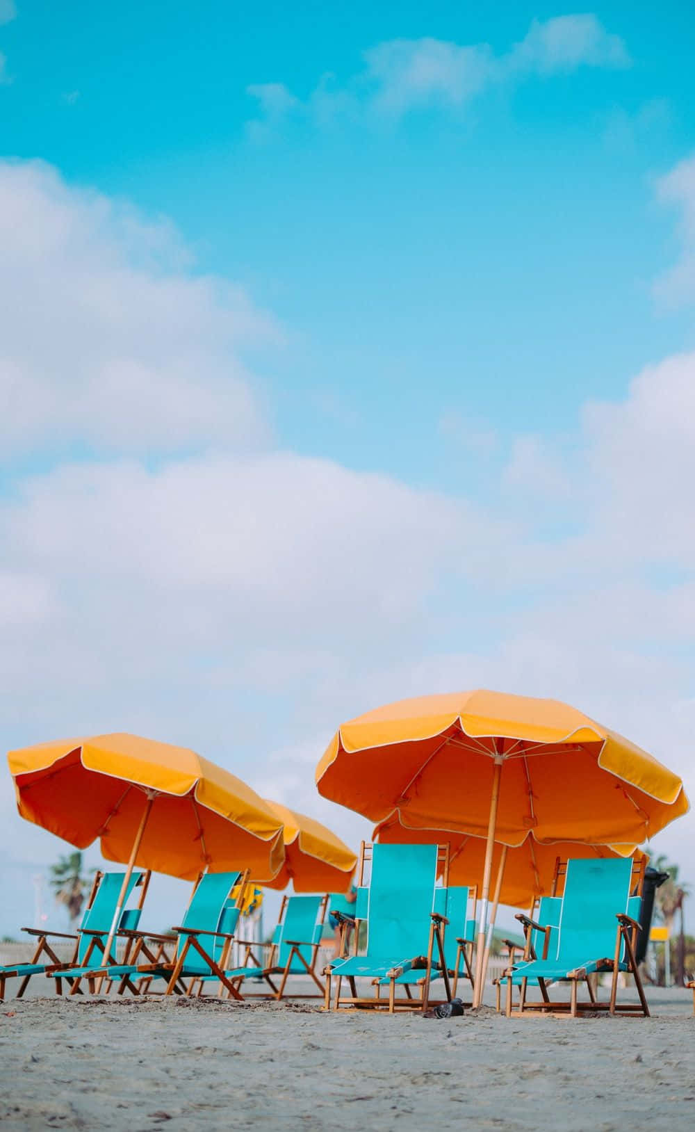 Beach Umbrella 桌布 壁紙 — 鮮豔的橙色遮陽傘和藍綠色躺椅點綴在陽光明媚的沙灘上，上方是明亮的藍天和蓬鬆的白雲。