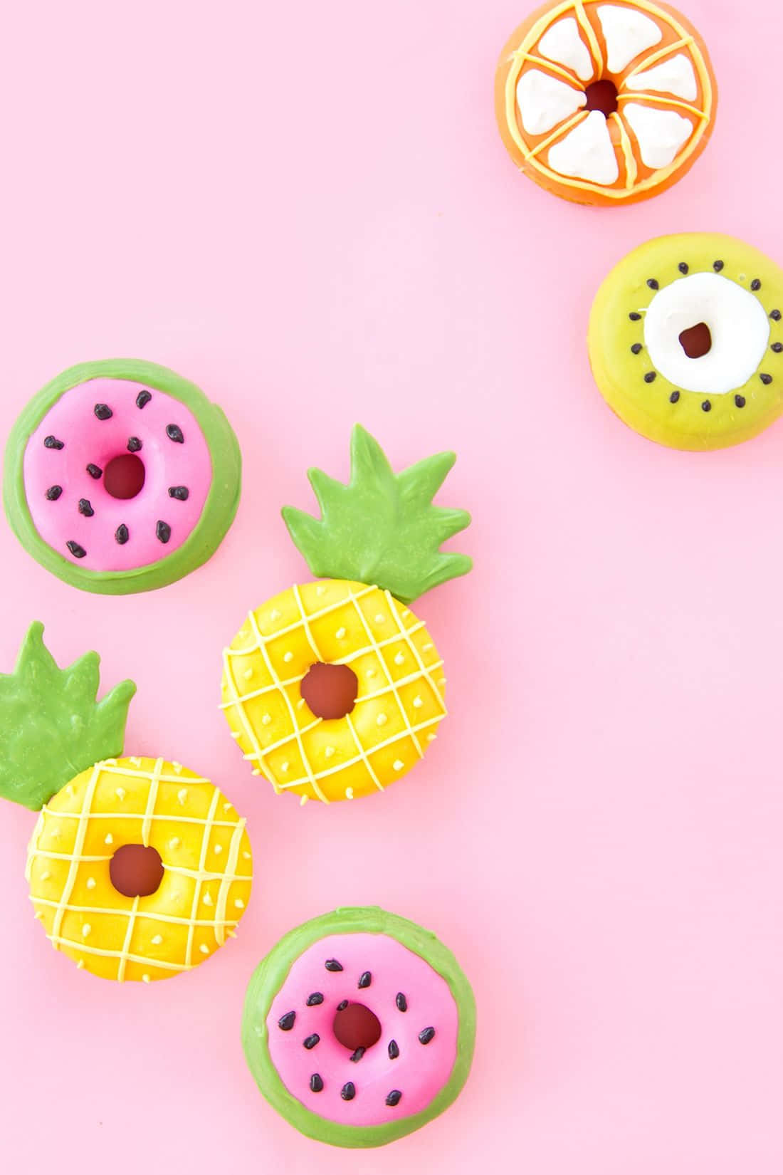 Cute Donut 桌布 壁紙 — 鮮豔的水果主題甜甜圈，造型為西瓜、鳳梨、奇異果和柳橙，排列在柔和的粉紅色背景上。