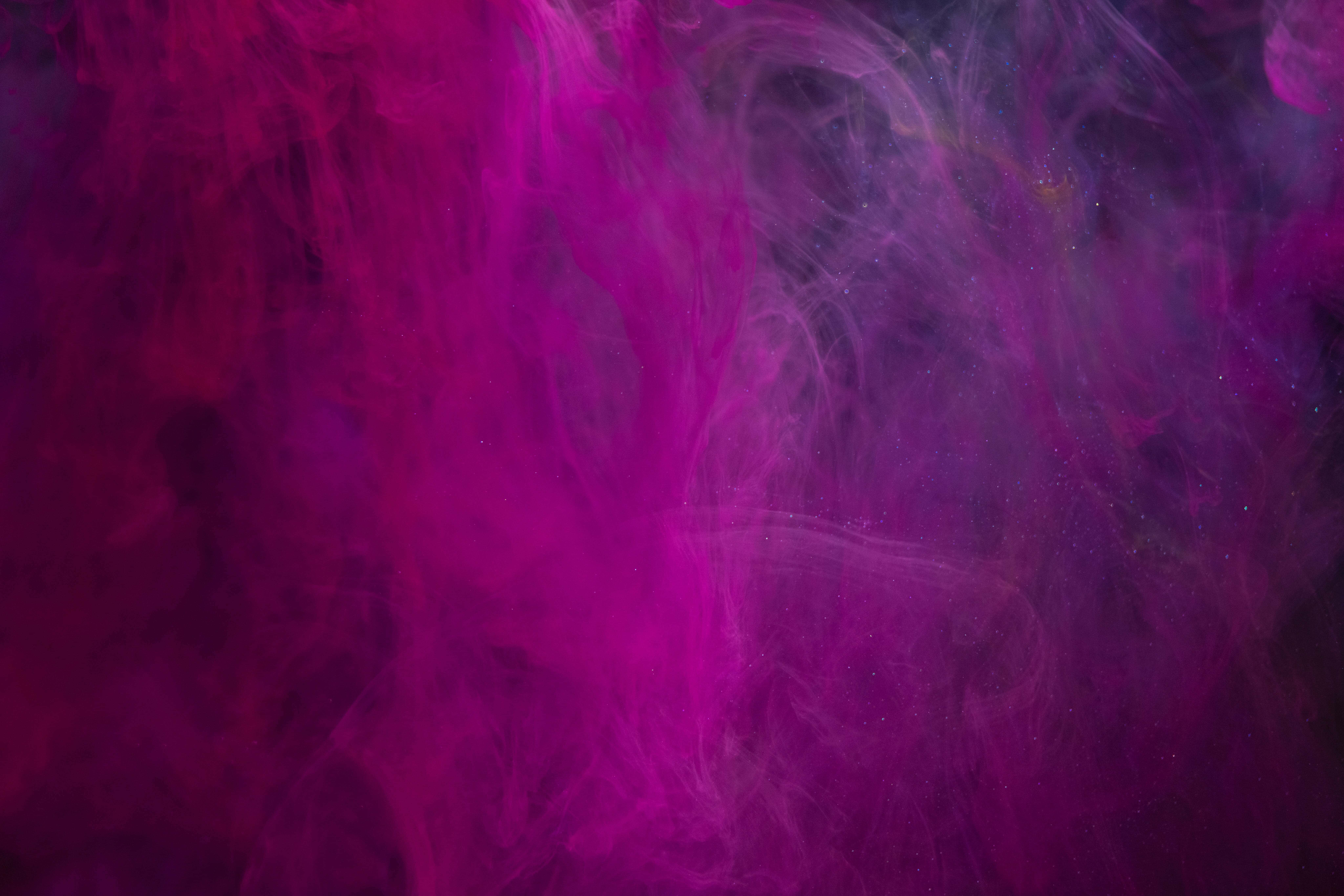 Pink Smoke 桌布 壁紙 — 鮮豔的洋紅色墨水在暗水中旋轉，形成帶有閃爍粒子的抽象流體運動。