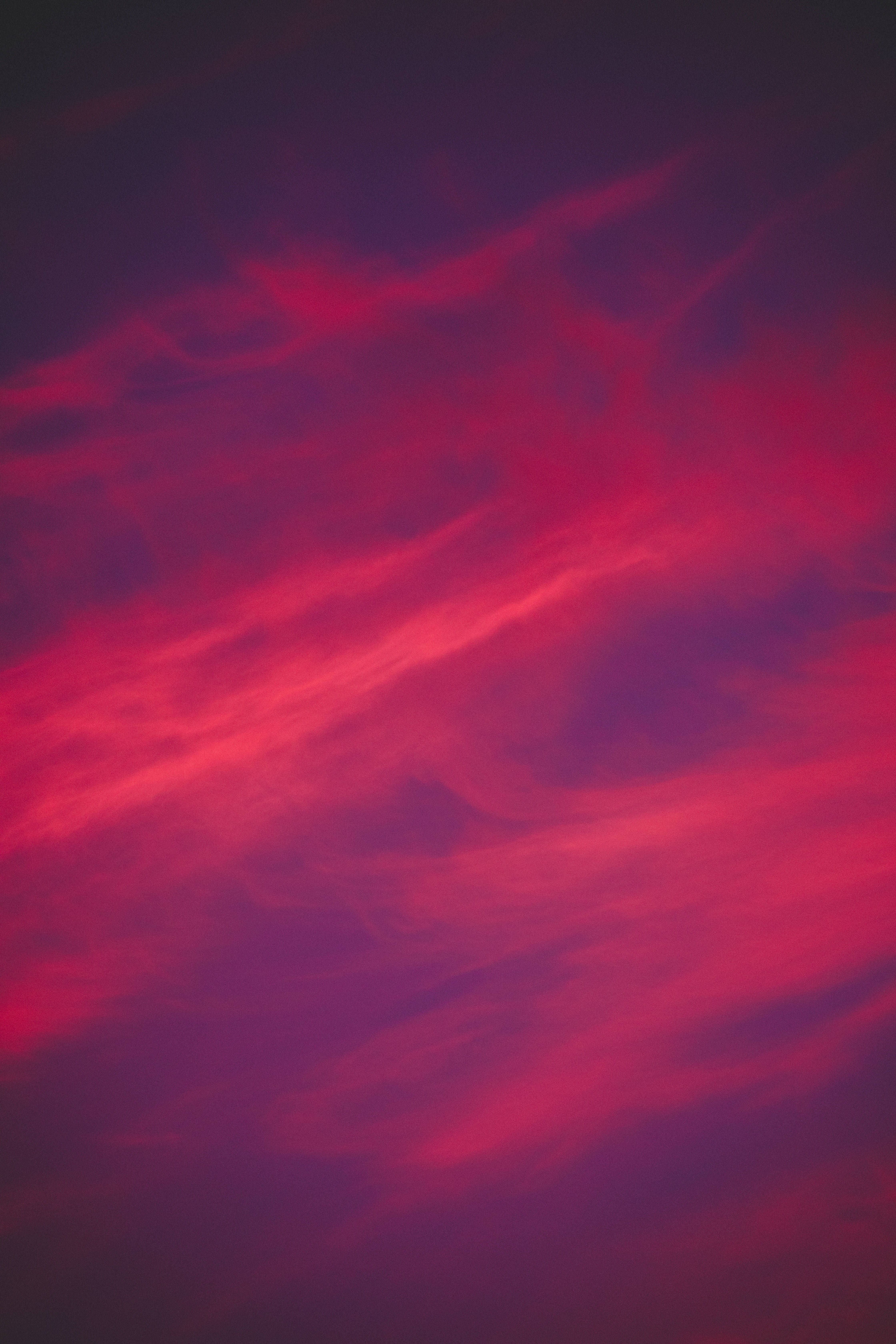 粉紅色 iPhone 桌布 壁紙 — 鮮豔的深紅色和洋紅色雲彩劃過暗紫色的天空，形成戲劇性的暮色場景。