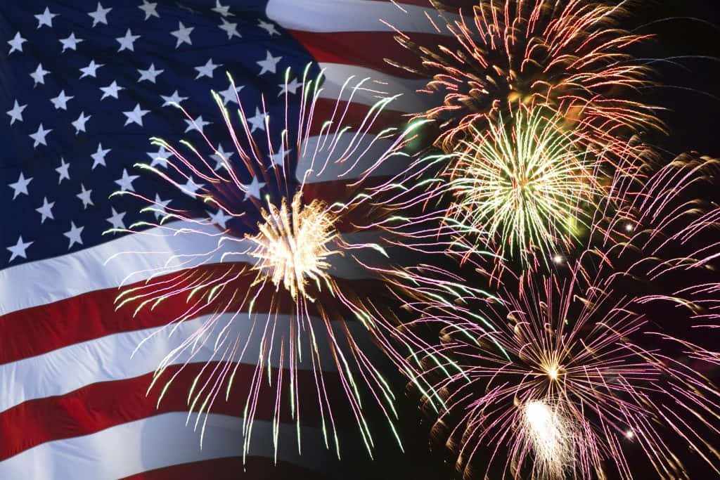 Happy Fourth Of July 桌布 壁紙 — 鮮豔的煙火在夜晚對著飄揚的美國國旗爆炸，營造出愛國慶祝場景。