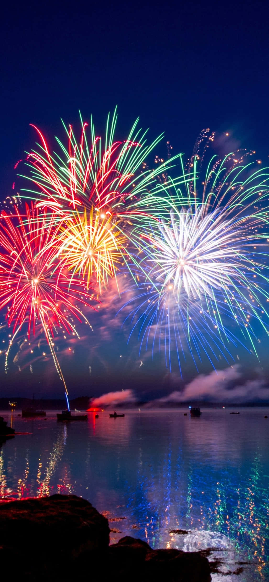 Fireworks 桌布 壁紙 — 鮮豔的煙火在平靜的水面上爆炸出燦爛的紅色、綠色和藍色，反射出耀眼的光芒。