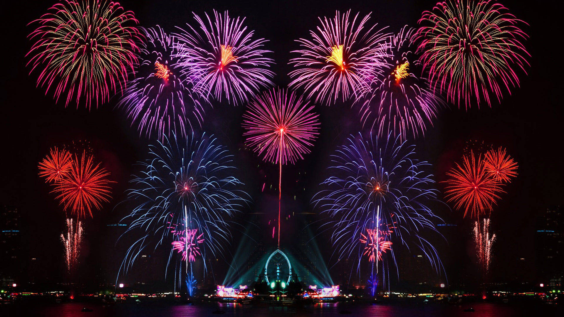 Fireworks 桌布 壁紙 — 鮮豔的煙火在深色城市景觀上空綻放出耀眼的紅色、紫色和藍色，倒映在下方水面。