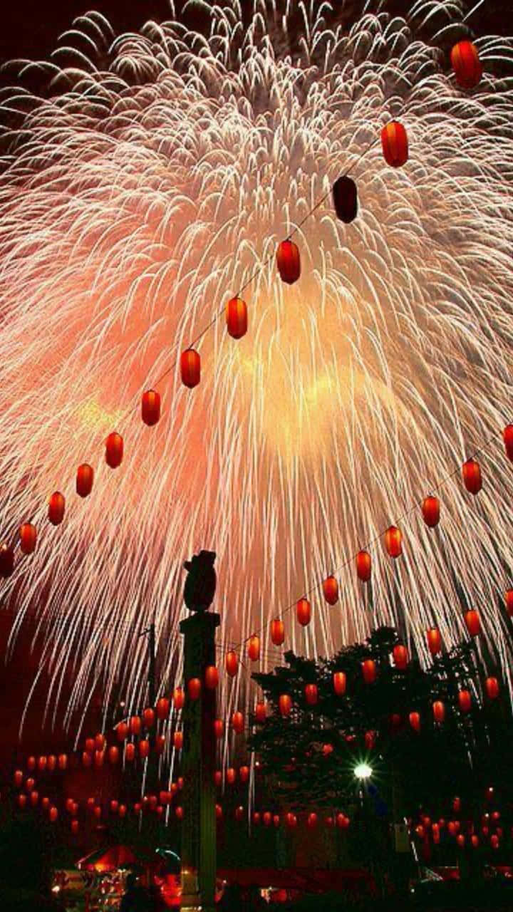 新年 桌布 壁紙 — 鮮豔的煙火在黑暗的夜空中，在閃爍的紅燈籠串上方綻放。