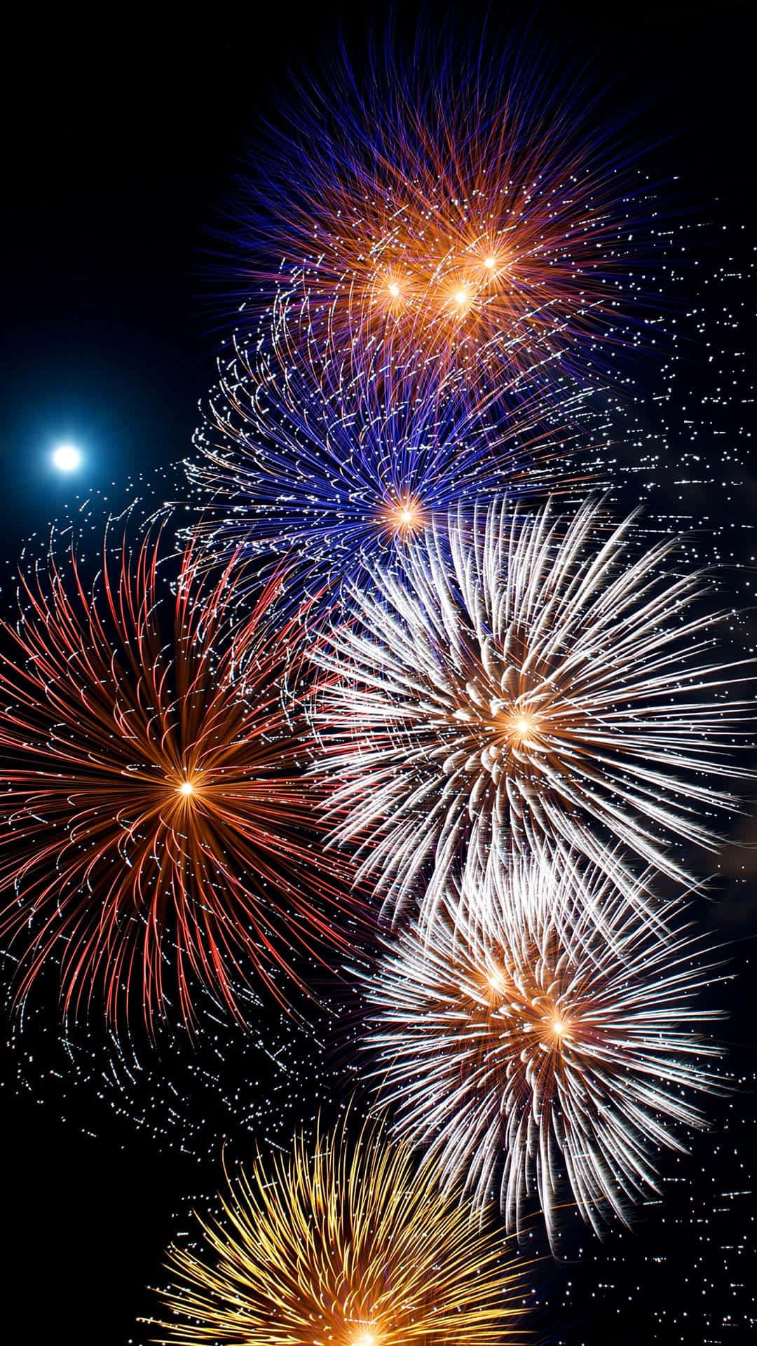彩色動圖 桌布 壁紙 — 鮮豔的煙火在黑暗的夜空中綻放出紅色、藍色、白色和金色的耀眼火花，伴隨著一輪明亮的月亮。