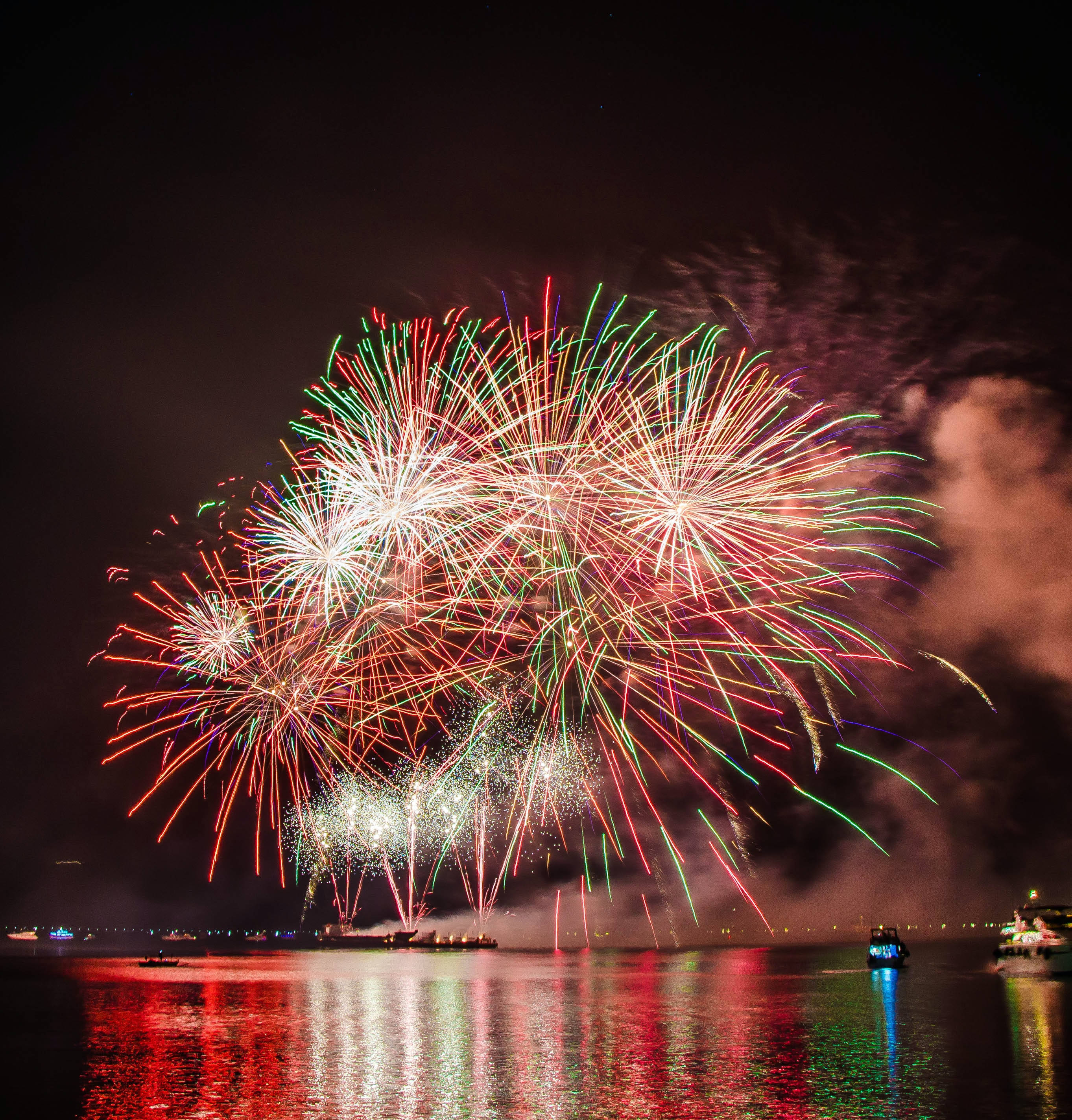 Fireworks 桌布 壁紙 — 鮮豔的煙火在黑暗的水面上綻放出耀眼的紅色、綠色和白色光芒，反射出它們燦爛的光輝。