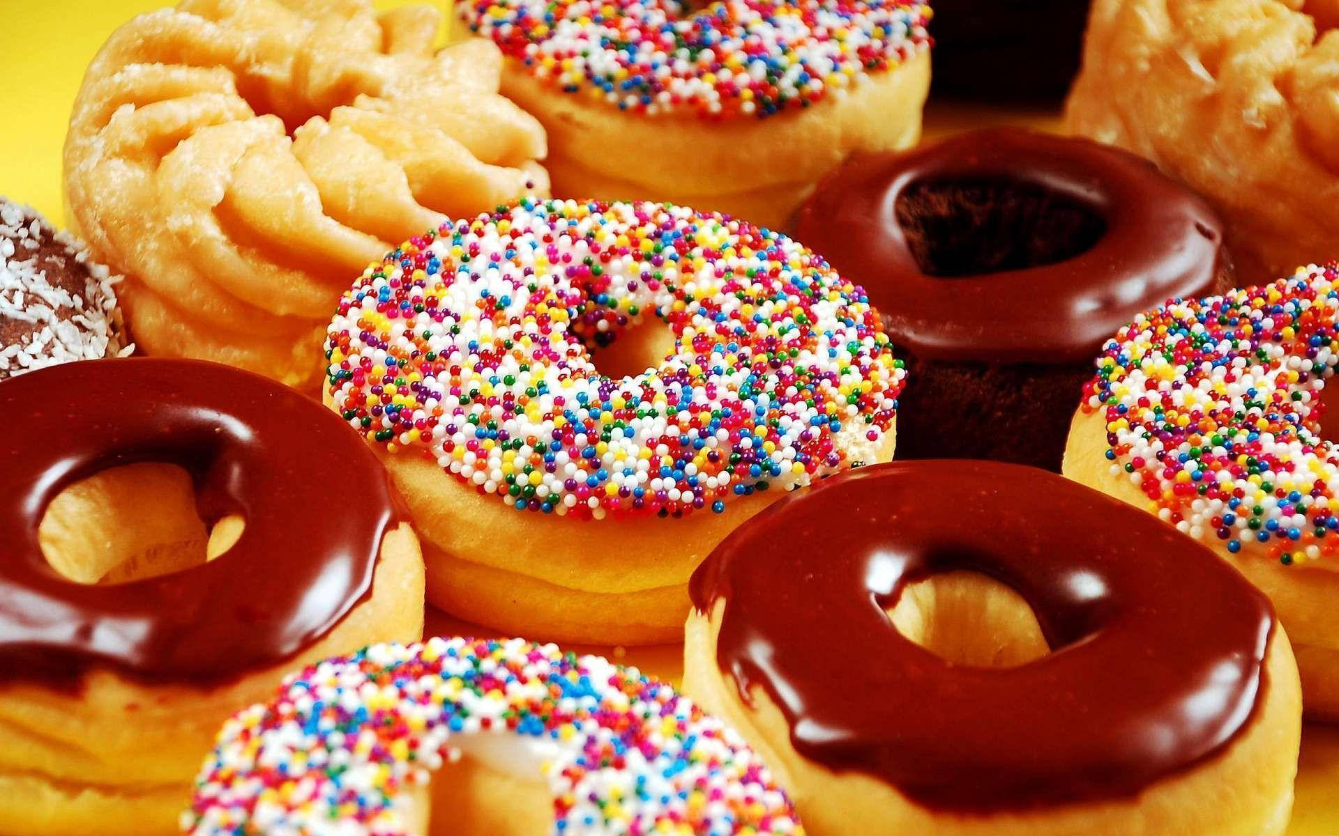 Donut 桌布 壁紙 — 鮮豔的特寫鏡頭，展示各種帶有巧克力糖霜和彩虹糖針的甜甜圈，背景為亮黃色。