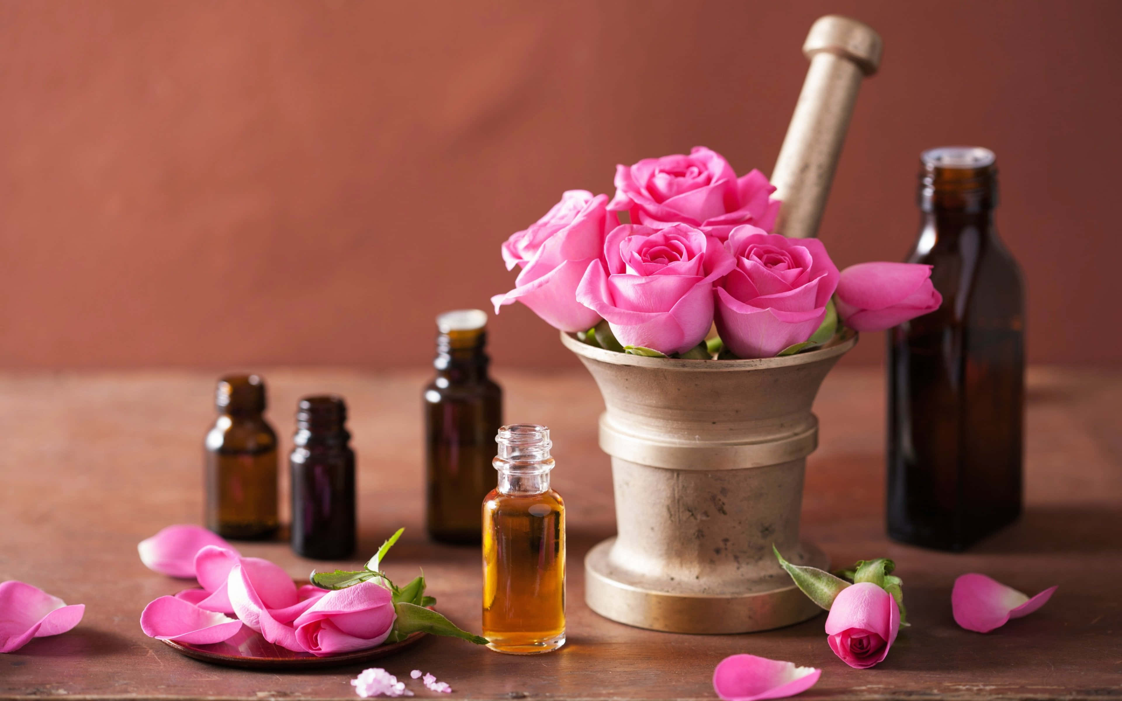 Spring Perfume 桌布 壁紙 — 鮮豔的粉紅玫瑰在黃銅研缽中盛開，旁邊是琥珀色的精油瓶，放在質樸的木桌上。