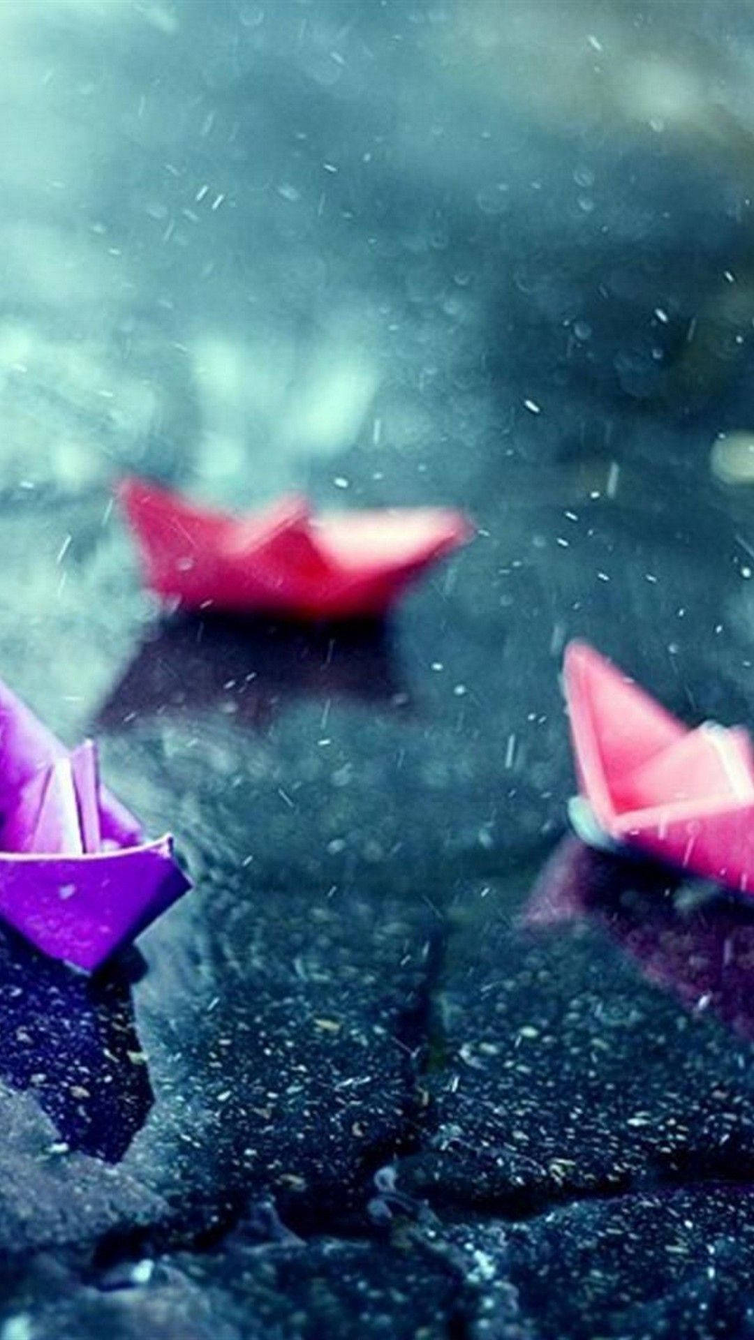 桌布 壁紙 — 鮮豔的粉紅色和紫色紙船在雨水浸濕的黑暗表面上輕輕漂浮，落下的水滴營造出憂鬱的氛圍。