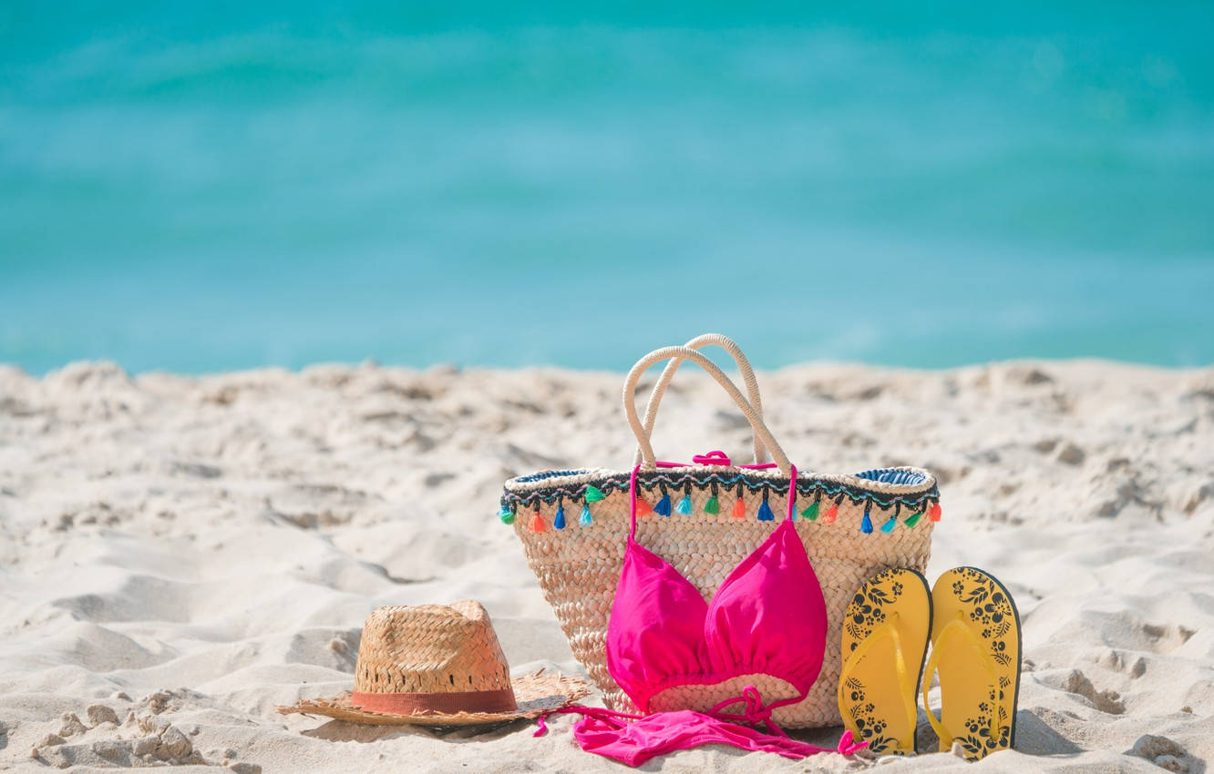 Beach Vacation 桌布 壁紙 — 鮮豔的粉紅色比基尼草帽和黃色夾腳拖放在白色沙灘上，旁邊是碧綠的海水。
