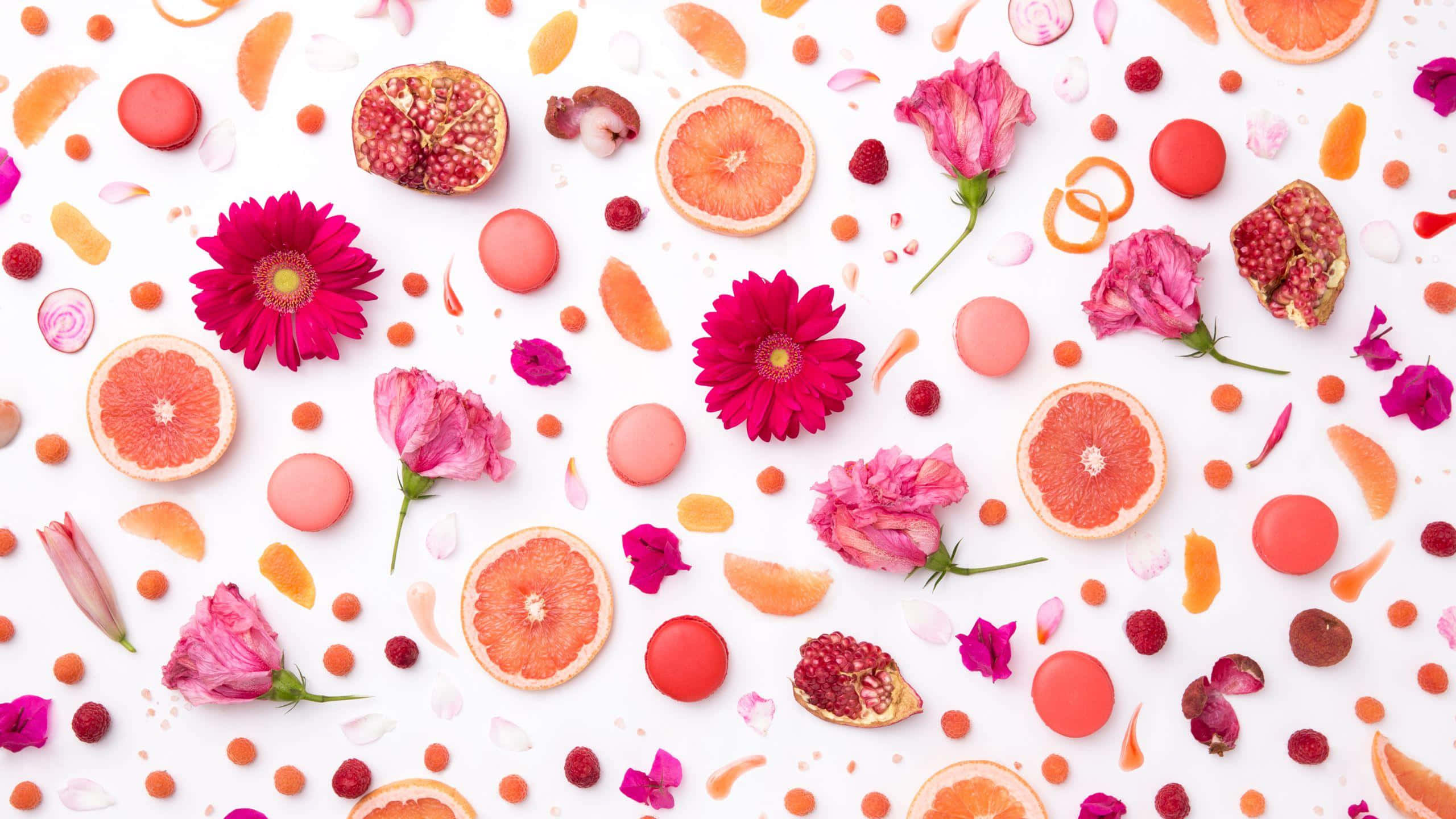 Fruits 桌布 壁紙 — 鮮豔的粉紅色花朵、柑橘片和馬卡龍散落在明亮的白色背景上，形成色彩繽紛的平鋪構圖。