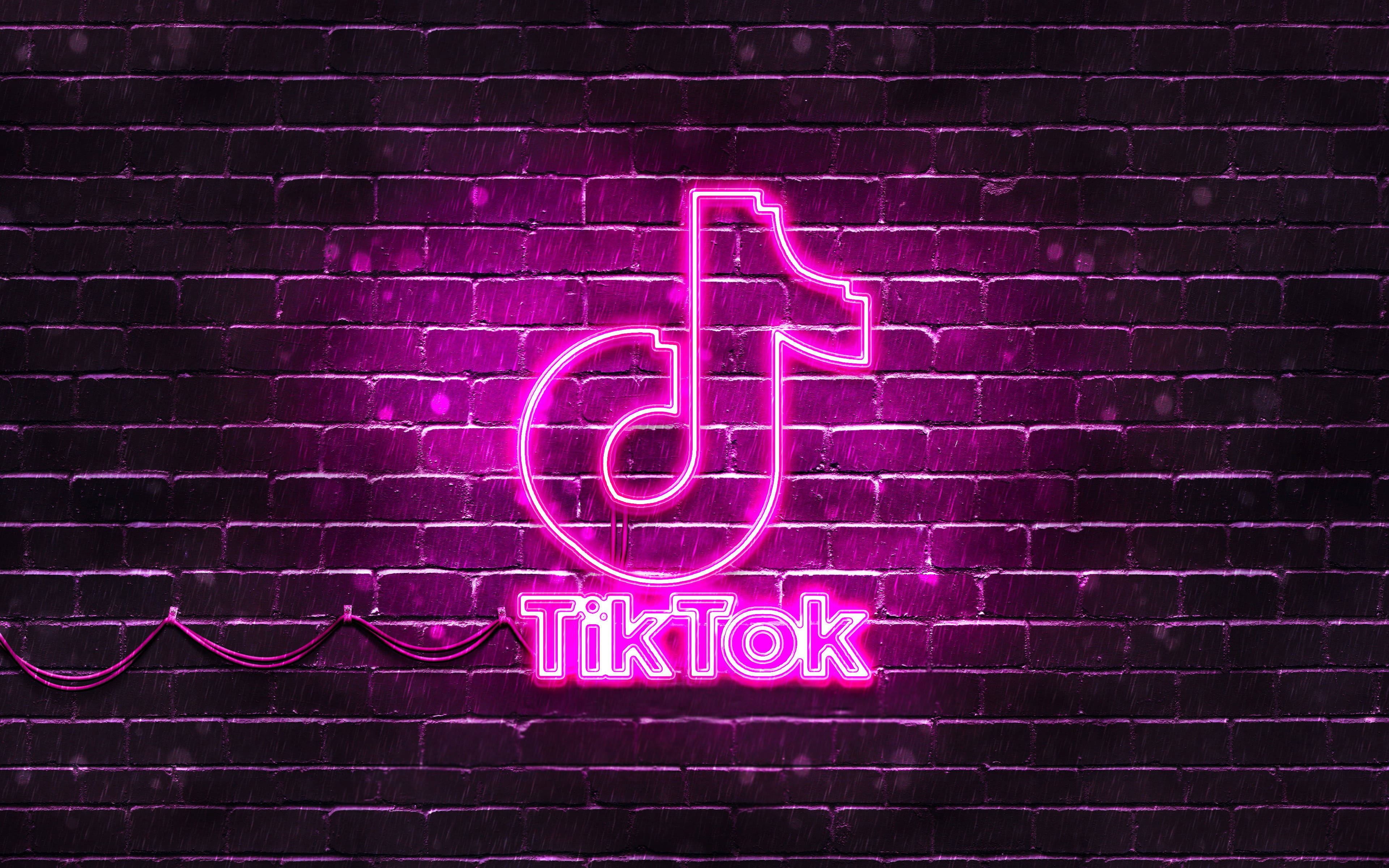 TikTok 動圖 桌布 壁紙 — 鮮豔的粉紅色霓虹燈TikTok標誌在夜雨中對著濕暗的磚牆發光。