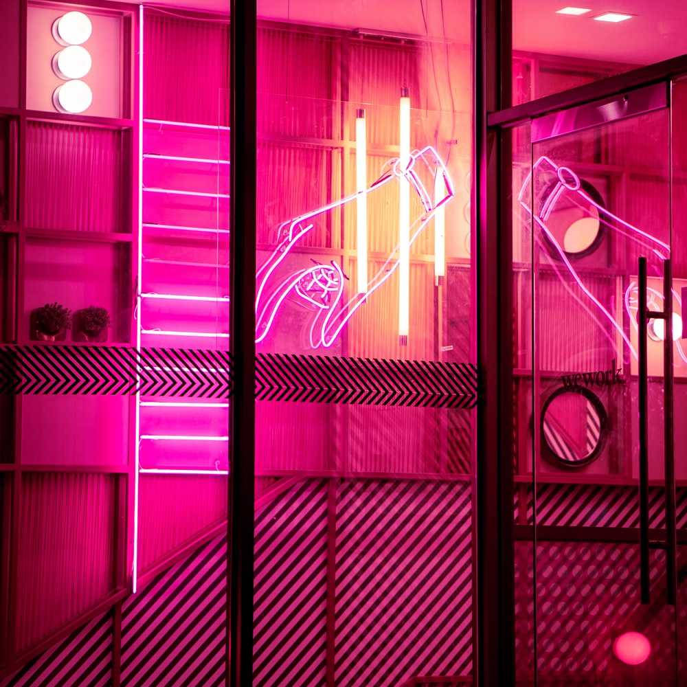 Hot Pink Aesthetic 桌布 壁紙 — 鮮豔的粉紅色霓虹燈在帶有幾何圖案和架子的現代玻璃牆上勾勒出雞尾酒杯的輪廓。