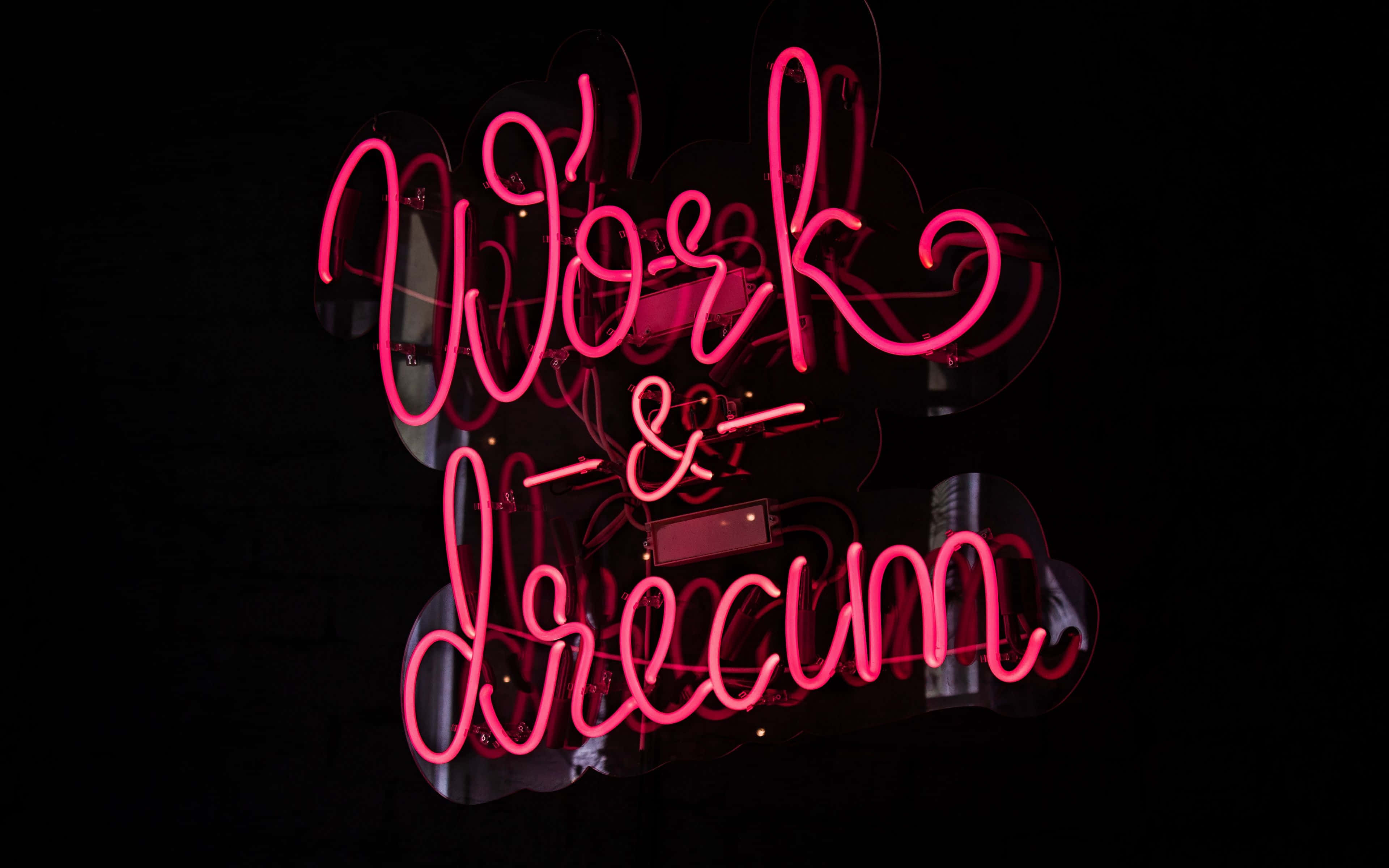 dreams 桌布 壁紙 — 鮮豔的粉紅色霓虹燈牌寫著「Work & Dream」，在漆黑的背景上發出光芒，帶有微妙的反射。