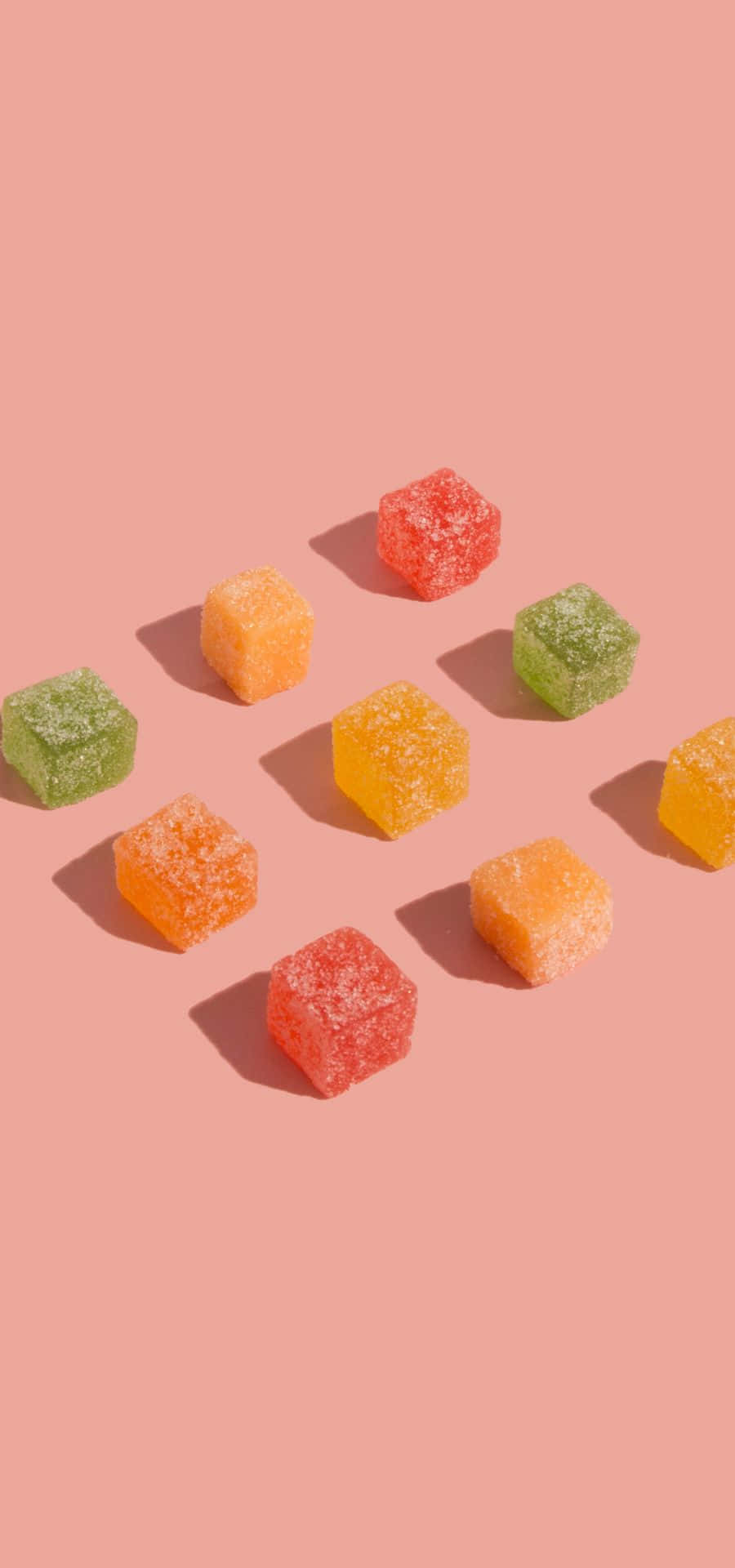 Peach Color 桌布 壁紙 — 鮮豔的糖衣軟糖方塊，紅色、橙色和綠色，散落在柔和的粉紅色背景上。