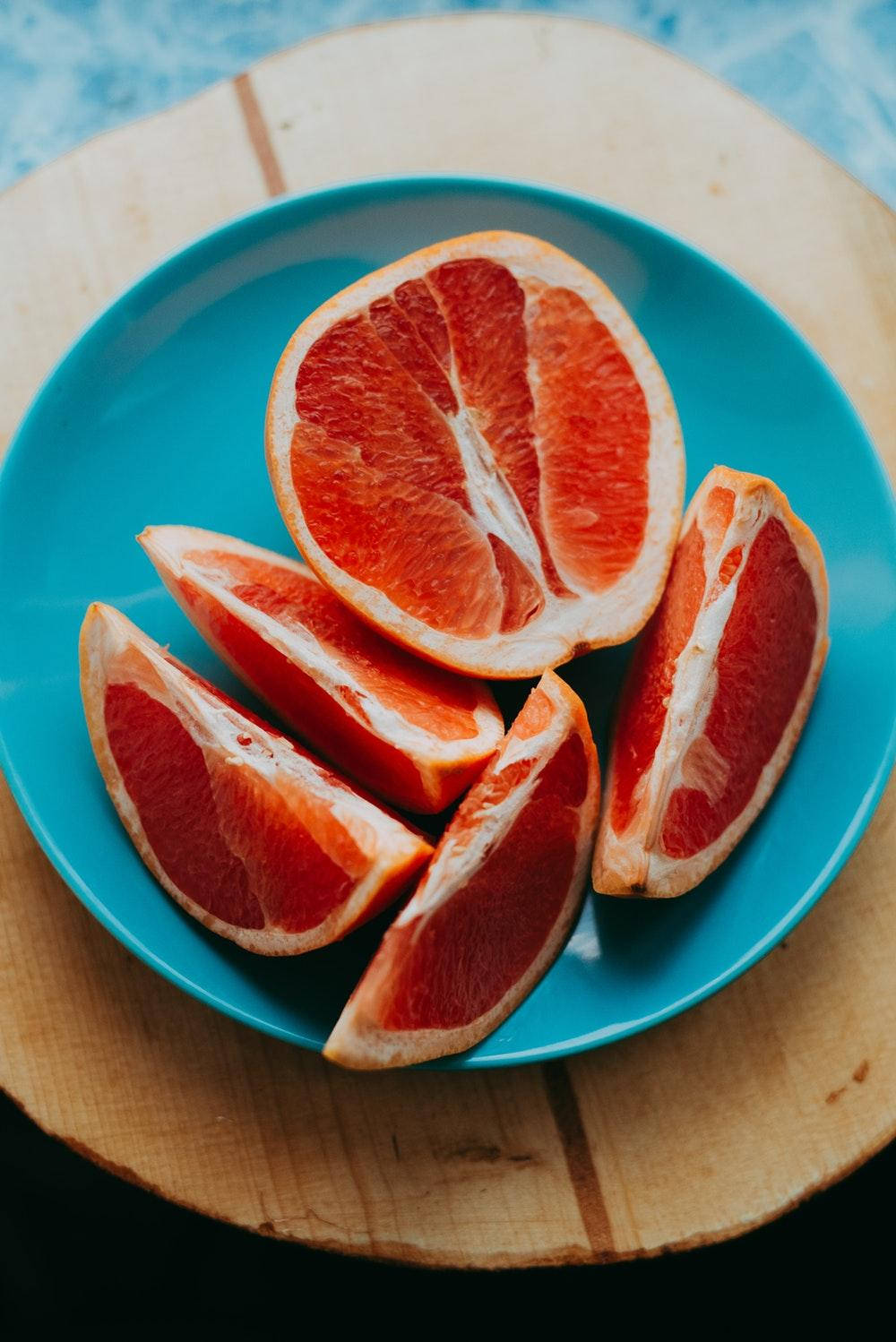 Healthy Food 桌布 壁紙 — 鮮豔的紅寶石色葡萄柚片排列在亮藍色盤子上，置於質樸木板上。