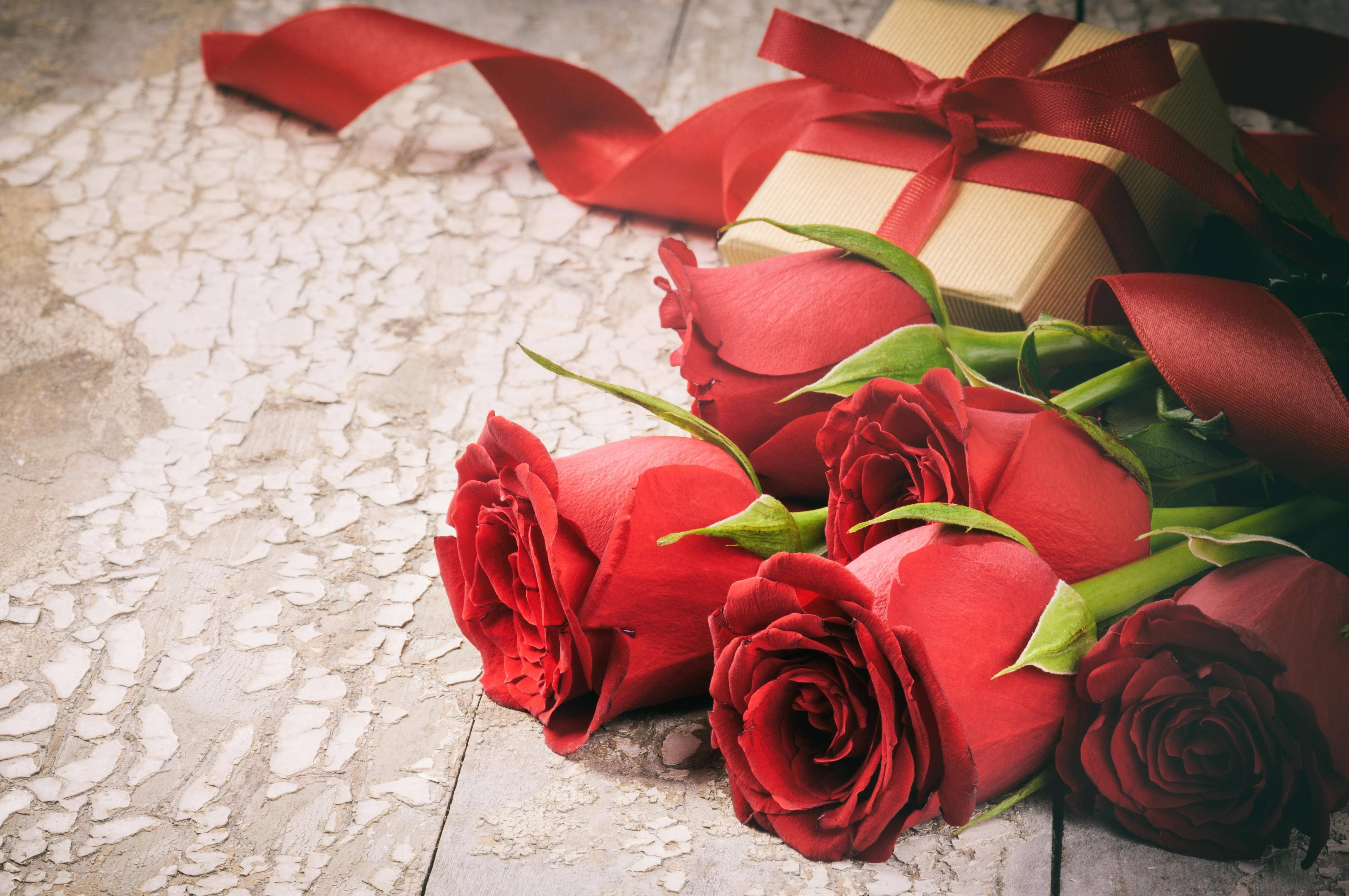 Red Roses 桌布 壁紙 — 鮮豔的紅玫瑰和一個用紅絲帶綁著的金色禮物盒，放在風化的木質表面上。