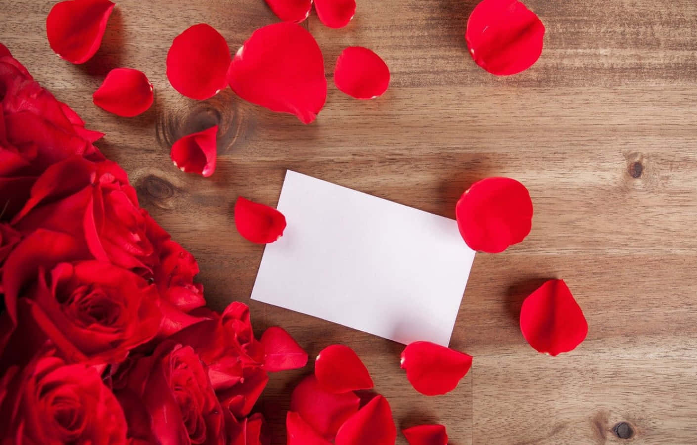 Rose Petal 桌布 壁紙 — 鮮豔的紅玫瑰和散落的花瓣圍繞著一張空白卡片，放在質樸的木質表面上。