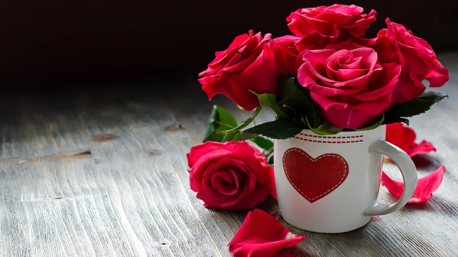 Roses Desktop 桌布 壁紙 — 鮮豔的紅玫瑰在一個帶有心形圖案的白色馬克杯中盛開，放在風化的木質表面上。