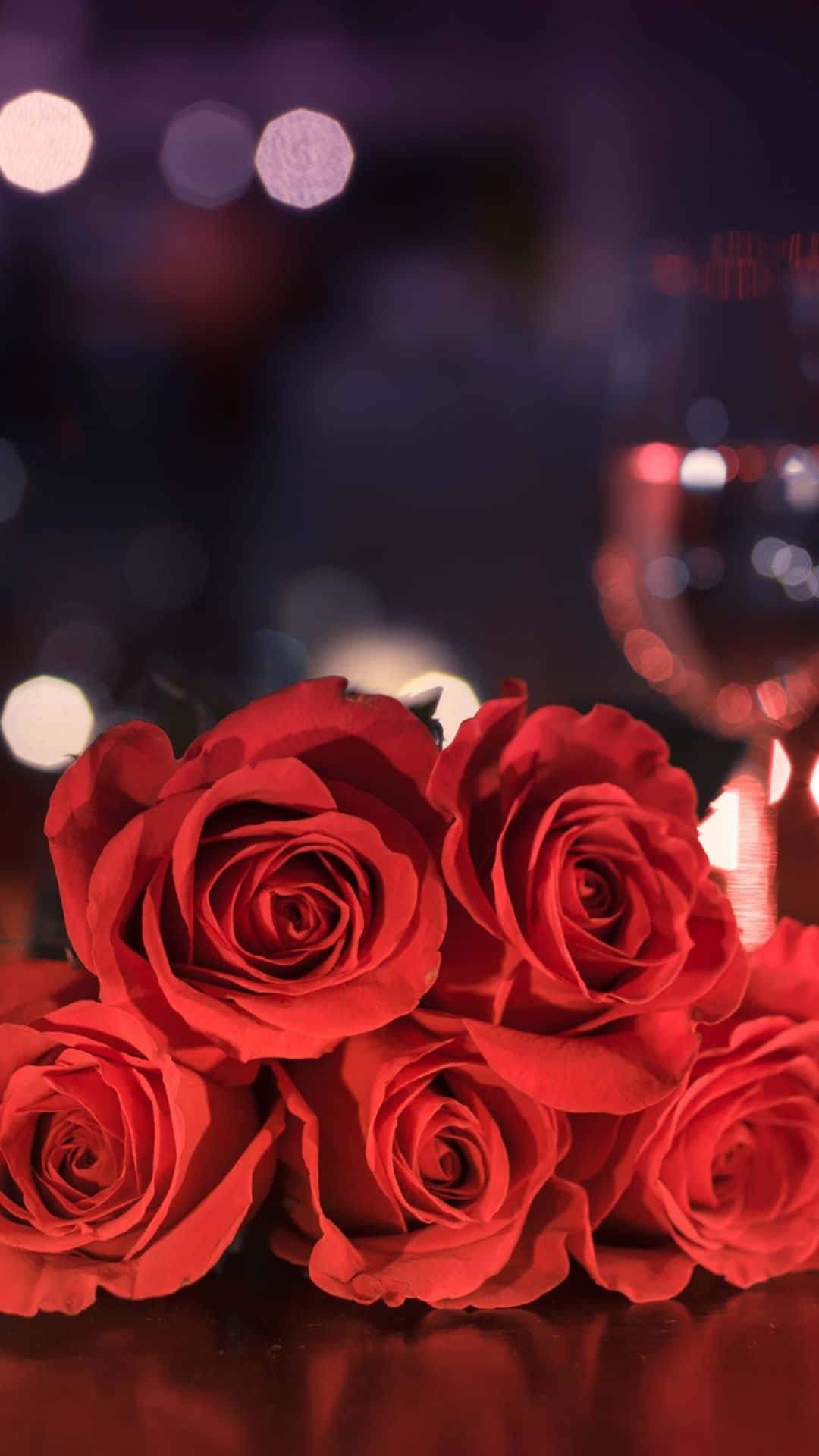 HD Rose 桌布 壁紙 — 鮮豔的紅玫瑰在柔和焦點中盛開，背景是溫暖燈光和酒杯營造的夢幻散景。