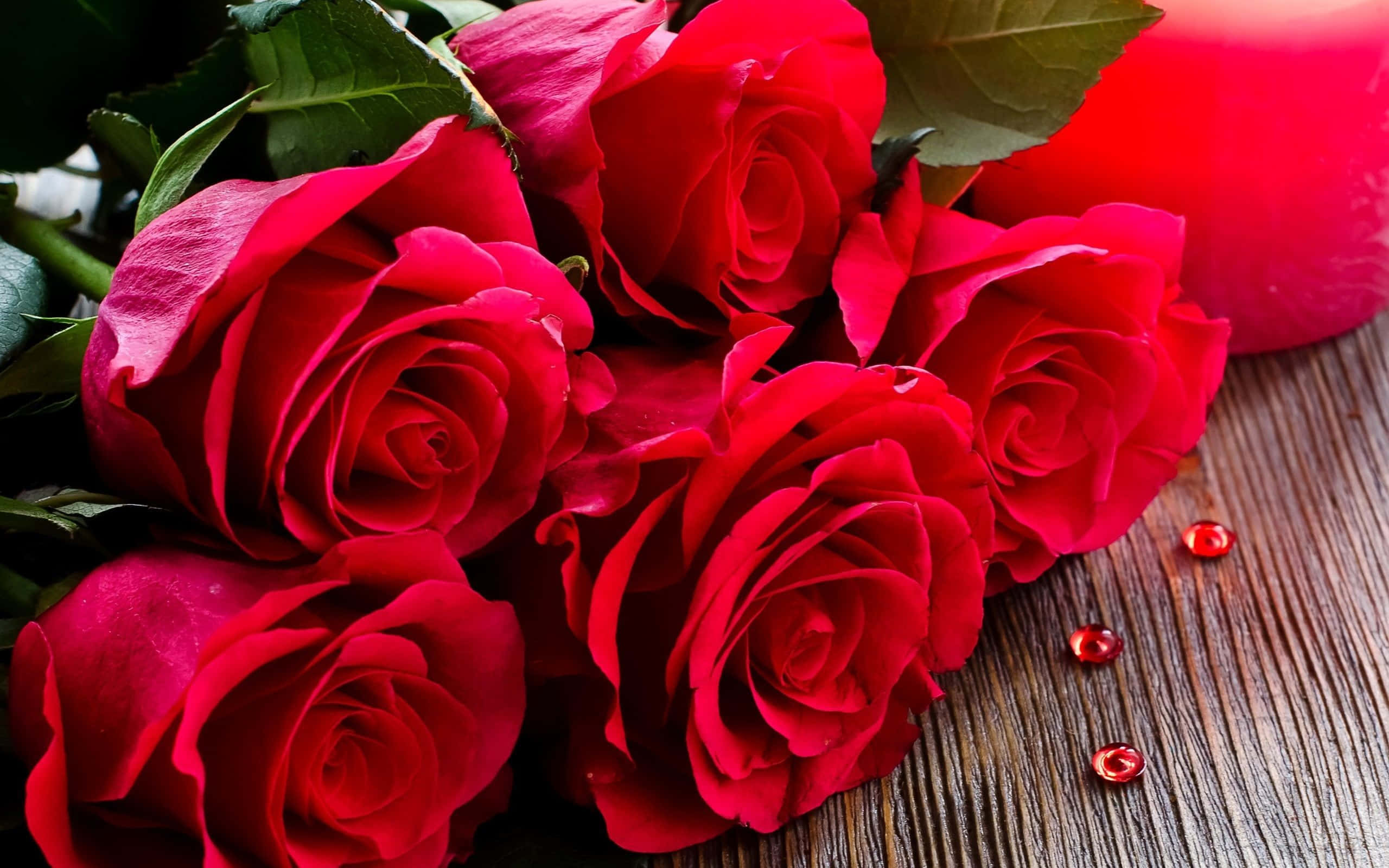 Bouquet 桌布 壁紙 — 鮮豔的紅玫瑰帶著露珠，放在質樸的木質表面上，旁邊有一支相配的紅蠟燭。