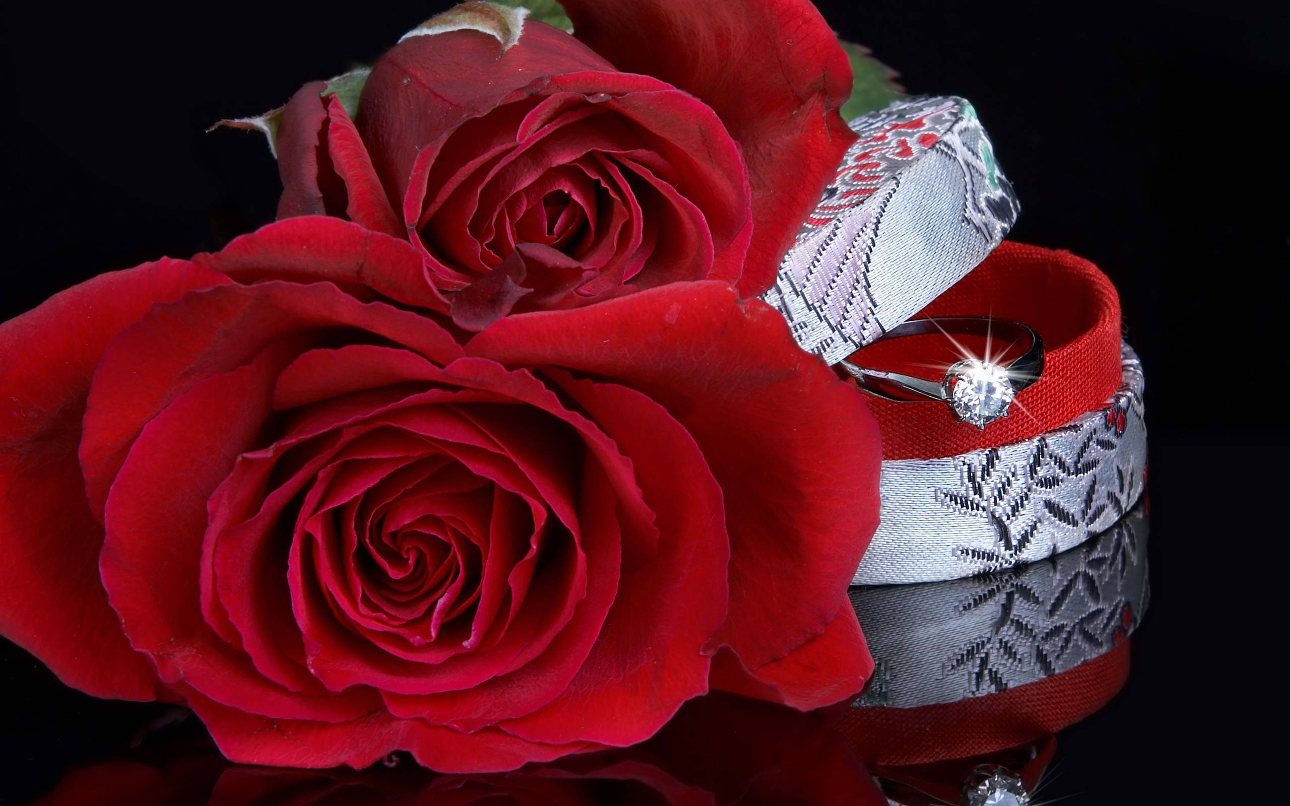 Wedding Aesthetic 桌布 壁紙 — 鮮豔的紅玫瑰環繞著一個打開的戒指盒，露出在反光黑色表面上閃閃發光的鑽石訂婚戒指。