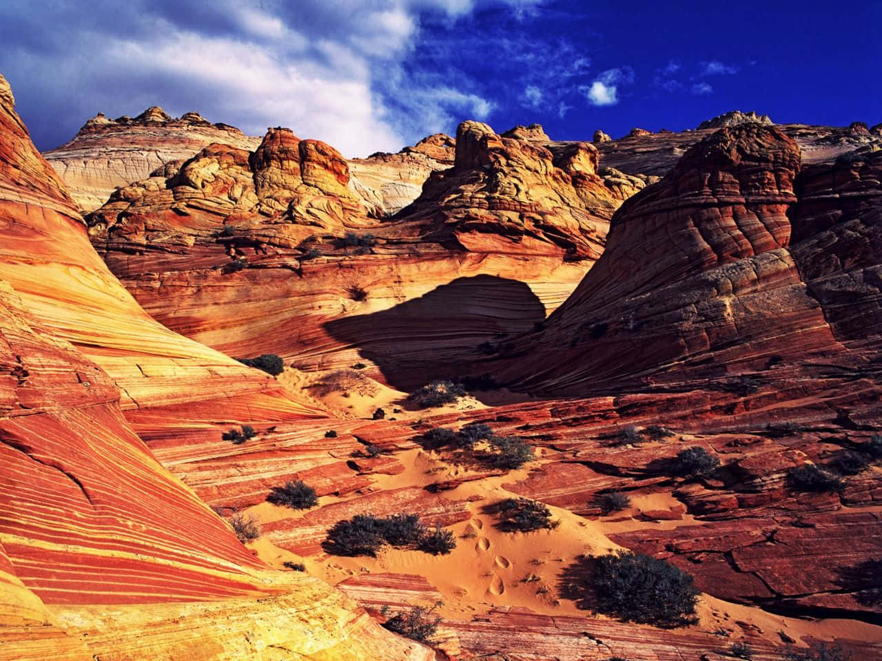Arizona 桌布 壁紙 — 鮮豔的紅色、橙色和黃色條紋岩層在深藍色天空和散落的雲朵下戲劇性地升起。