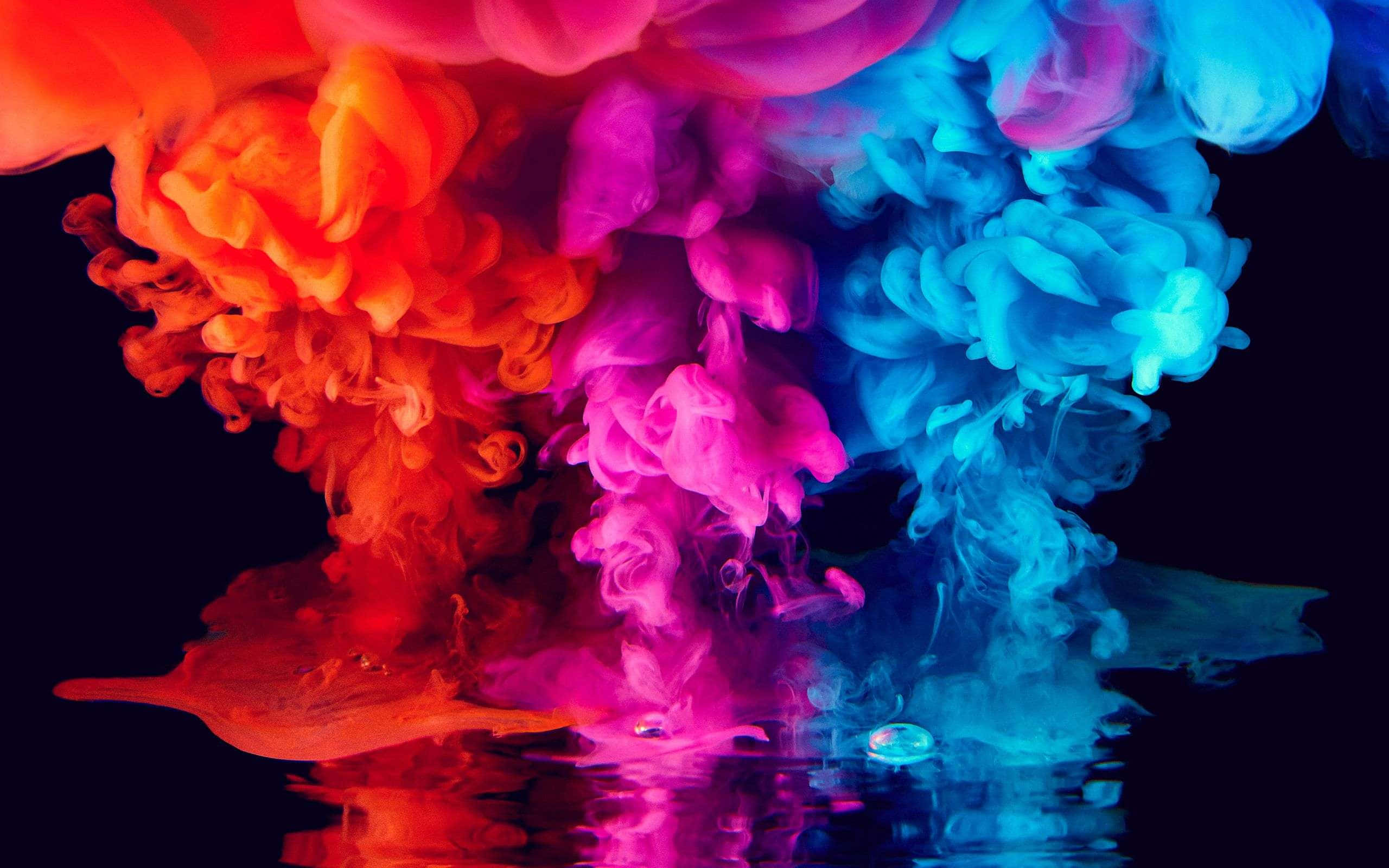 Colorful Smoke 桌布 壁紙 — 鮮豔的紅色、粉紅色和藍色墨水在黑色背景的水中戲劇性地旋轉，產生鮮明的倒影。