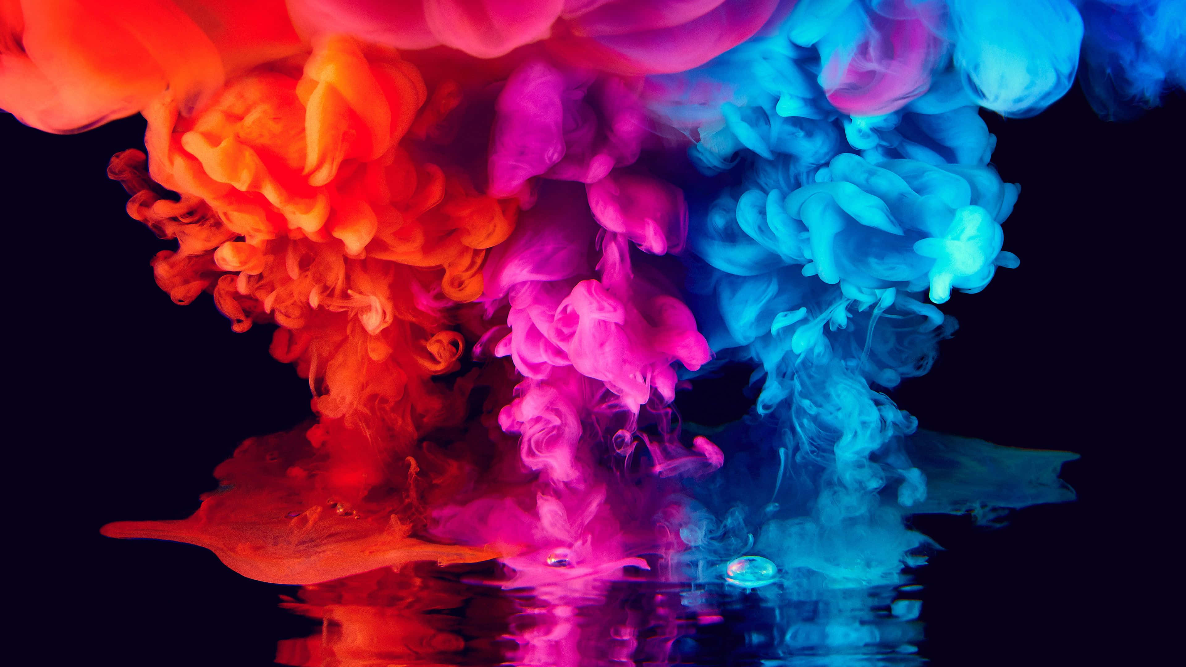 Colorful Aesthetic 桌布 壁紙 — 鮮豔的紅色、粉紅色和藍色墨水在黑色水中戲劇性地旋轉，創造出超現實的彩色爆炸。