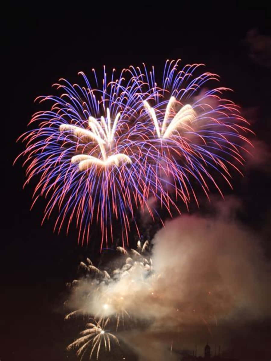 Celebration 桌布 壁紙 — 鮮豔的紅色、藍色和白色煙火在黑暗的夜空中綻放，下方煙霧繚繞，呈現出令人眼花撩亂的景象。
