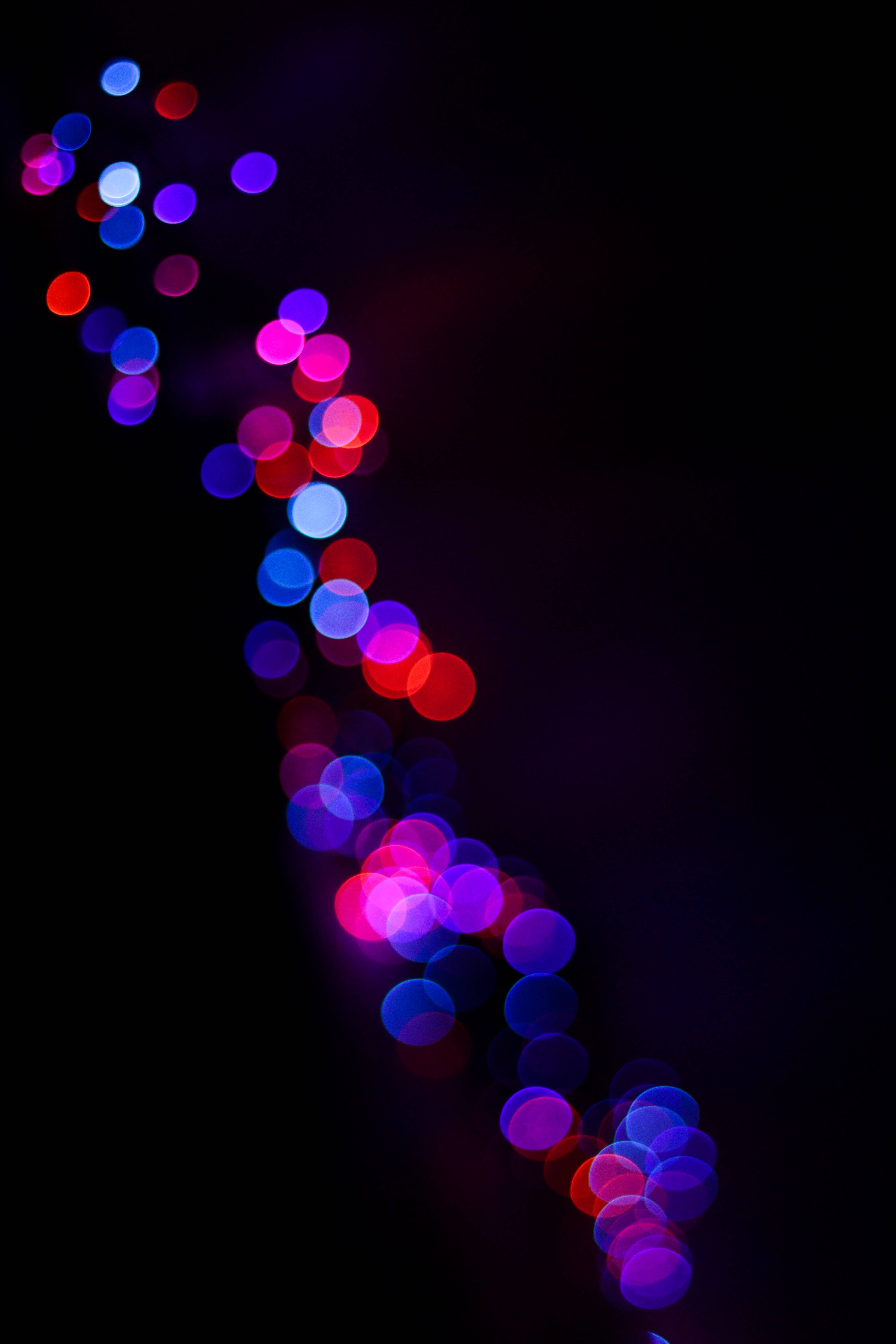 Bokeh 桌布 壁紙 — 鮮豔的紅色、藍色和紫色散景燈光以對角線瀑布形式在深黑色背景上發光。