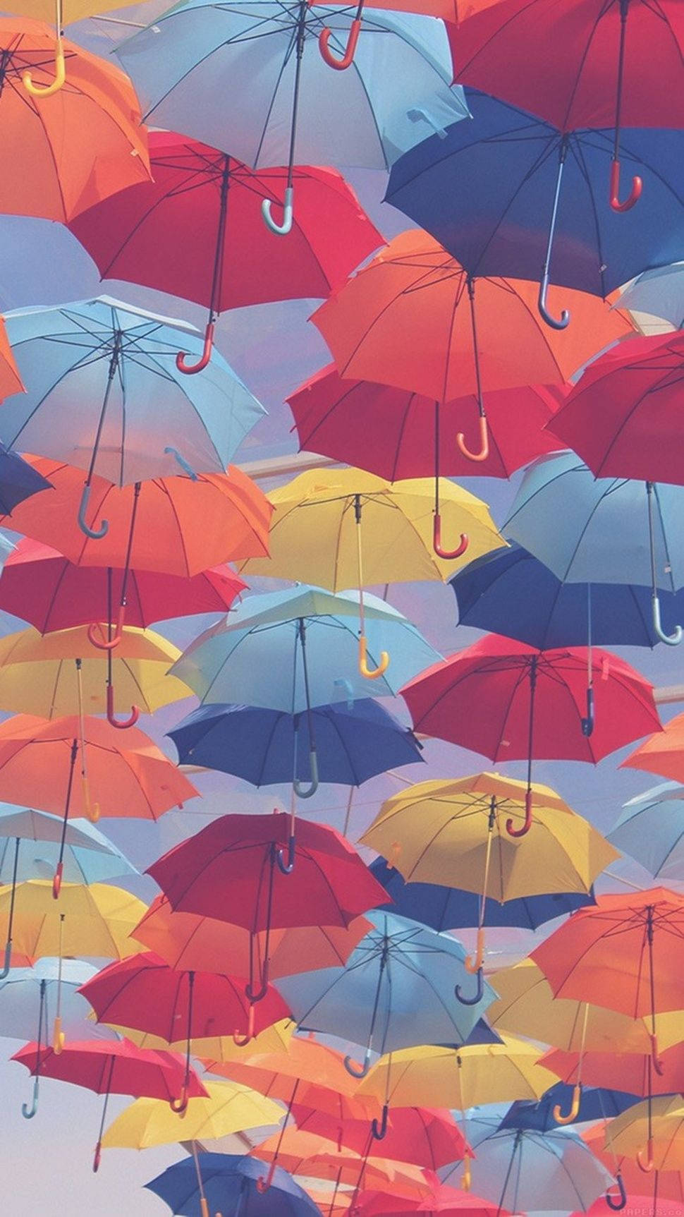 少女風 桌布 壁紙 — 鮮豔的紅色、黃色和藍色雨傘密集地漂浮在柔和的粉彩天空上，營造出一個奇特的華蓋。