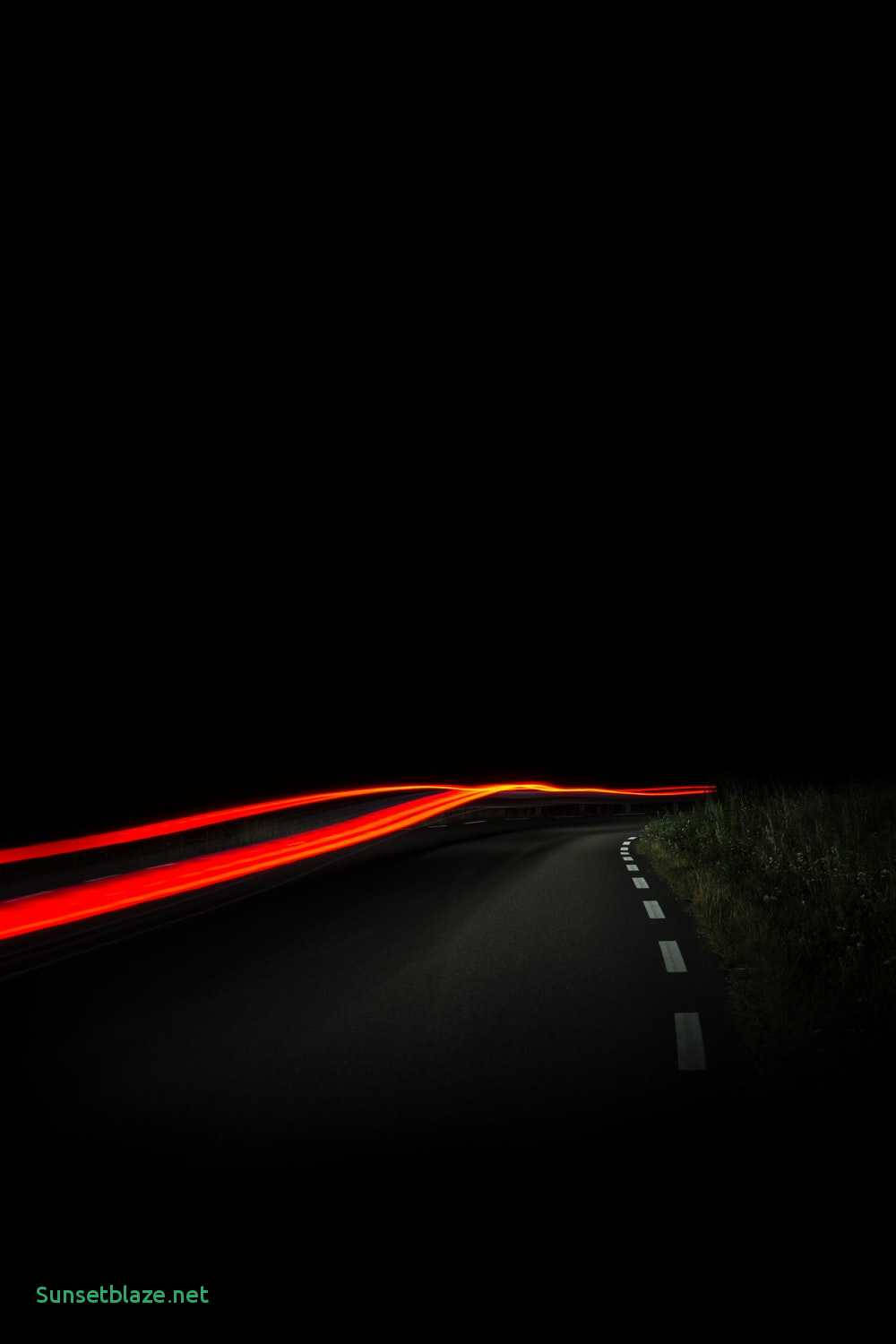 AMOLED 桌布 壁紙 — 鮮豔的紅色光軌沿著黑暗蜿蜒的道路在夜間延伸，由經過的車輛照亮。