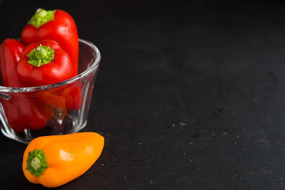 pepper 桌布 壁紙 — 鮮豔的紅色和橙色燈籠椒放在玻璃碗中，置於深色紋理表面上，景深較淺。