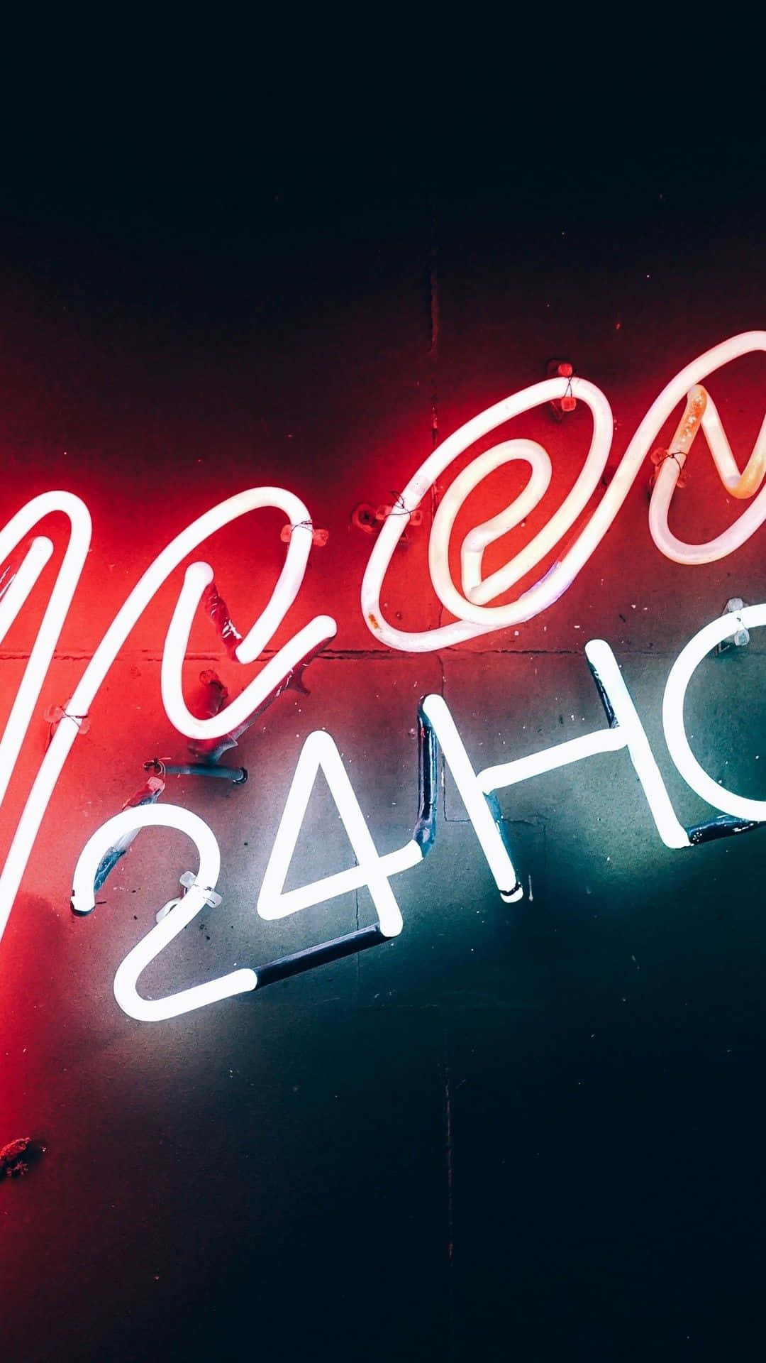 iPhone Neon 桌布 壁紙 — 鮮豔的紅色和白色霓虹燈字母在黑暗的牆壁上拼出 'NEON 24H'，在夜間城市環境中明亮發光。