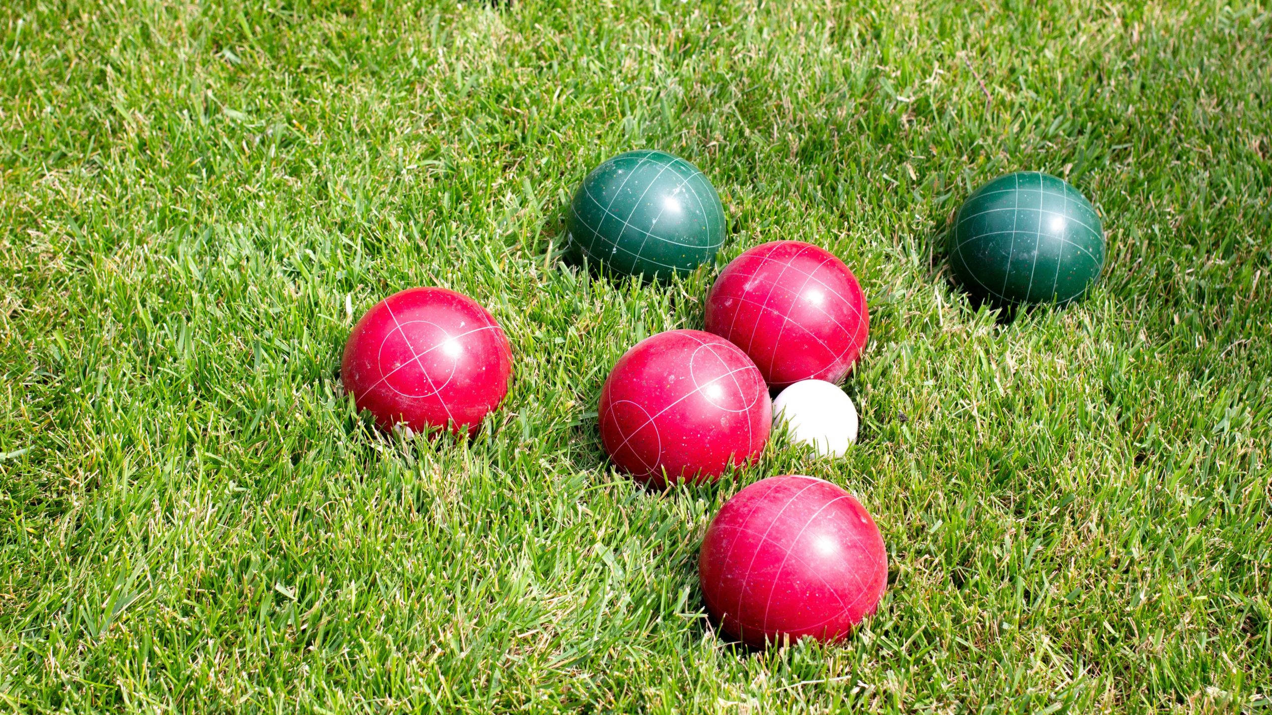 balls 桌布 壁紙 — 鮮豔的紅色和綠色草地滾球在明亮的陽光下放置在茂盛的綠色草地上。