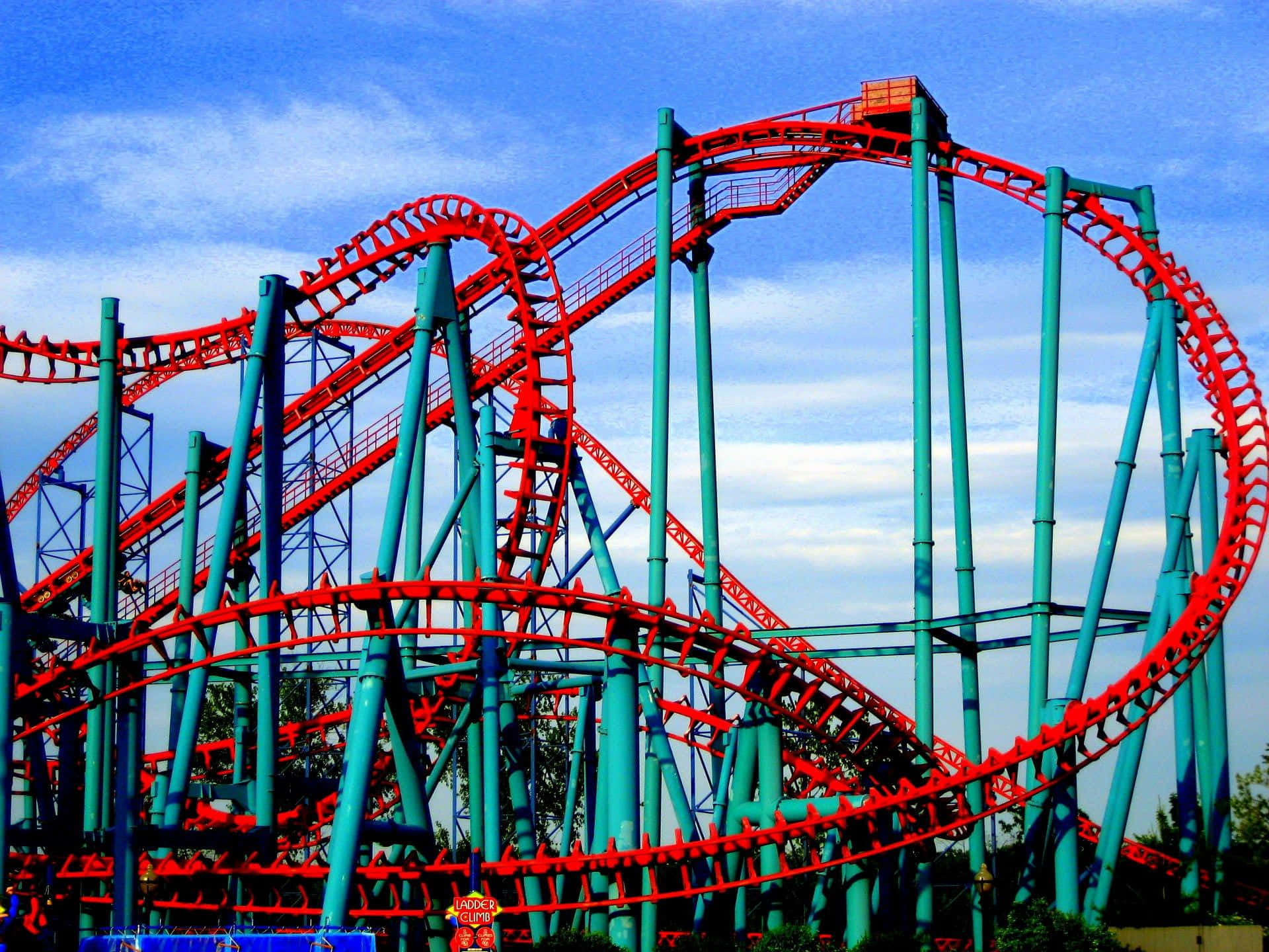 Roller Coaster 桌布 壁紙 — 鮮豔的紅色和藍綠色雲霄飛車在晴朗的藍天和白雲中扭轉和環繞。