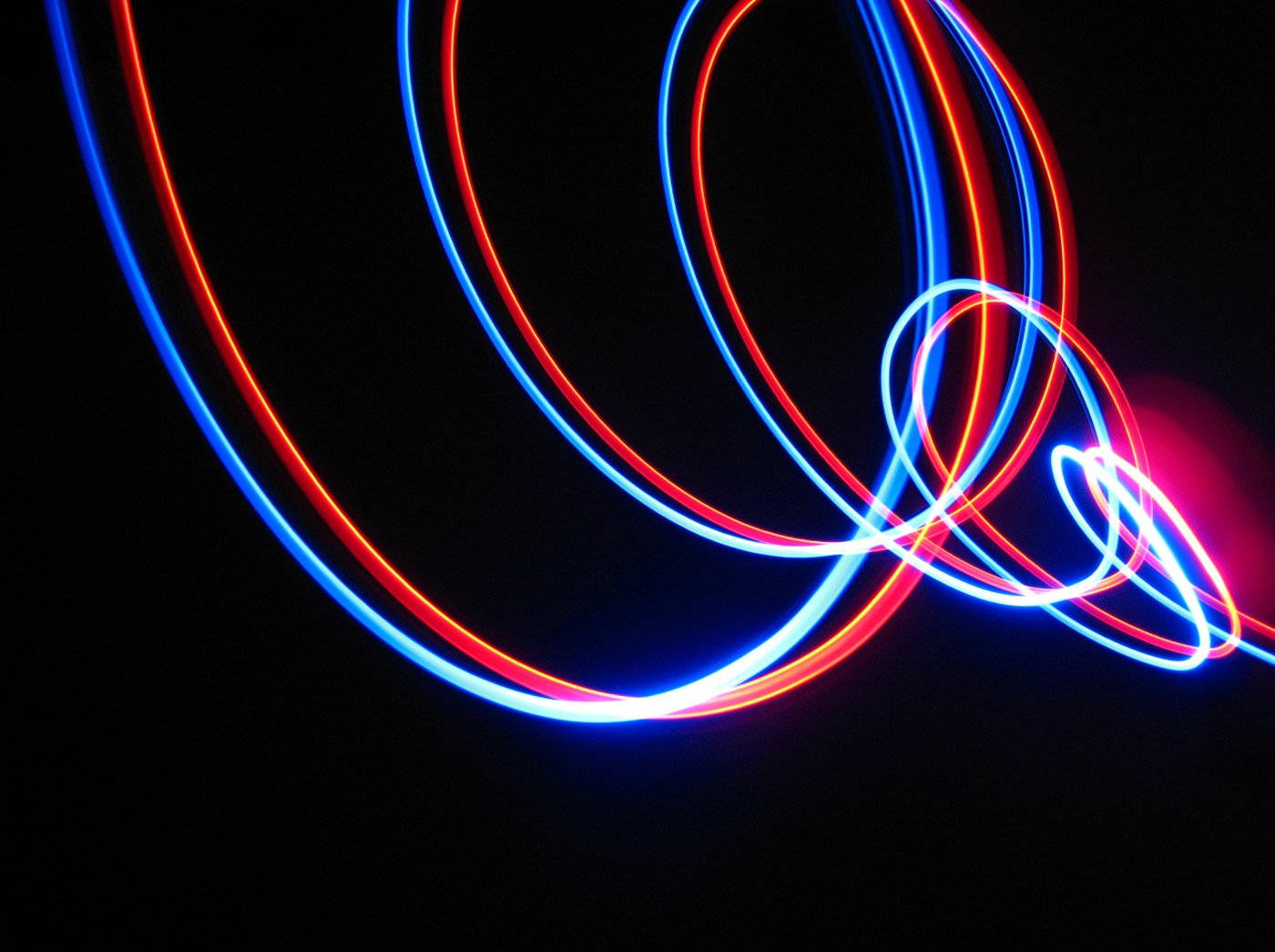 Neon Light 桌布 壁紙 — 鮮豔的紅色和藍色光軌在漆黑的背景上優雅地旋轉成環狀。